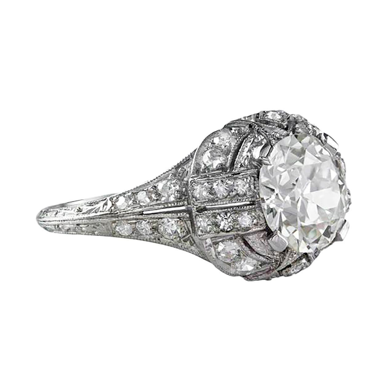 This antique engagement ring features a brilliant round diamond center stone weighing 1.97 carats certified by GIA as M color and VS1 in clarity, set in a platinum four prong setting. Accented by 34 brilliant round diamonds weighing 0.35 carats