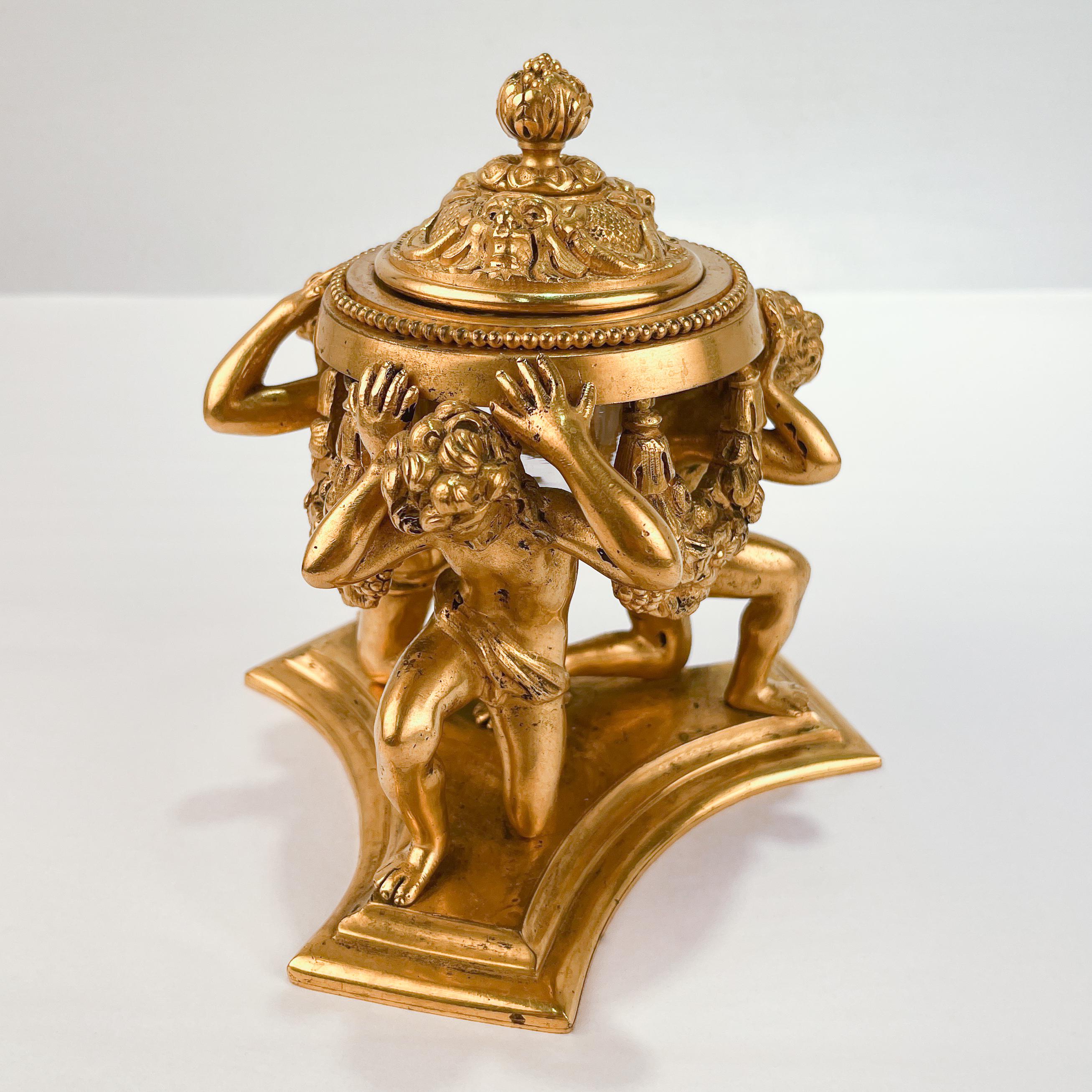 A fine antique bronze inkwell.

By E. F. Caldwell.

With a hinged top and glass inkwell insert supported by three kneeling youths on a trefoil base. 

Marked to the base with a Caldwell factory mark.

Simply a wonderful