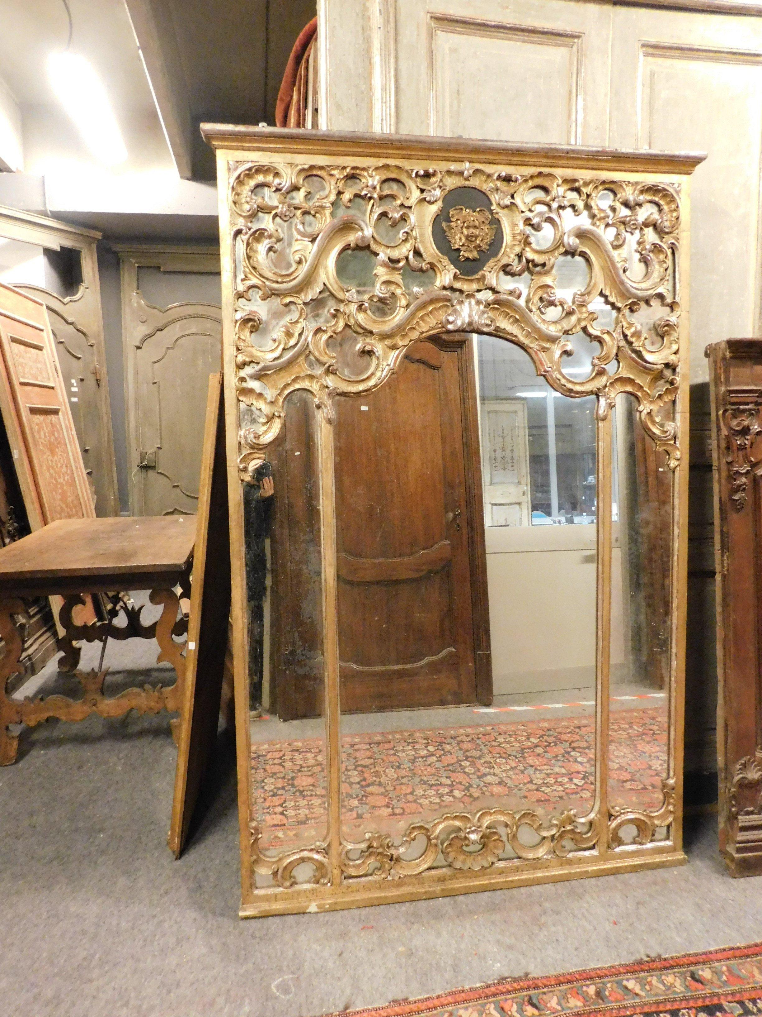 Antique mirror in gilded wood, with many curls and decorations, richly carved with central putto on black lacquered round, original leaf gilding, with beautiful patina produced over the centuries, mirror in excellent condition, built in the 18th