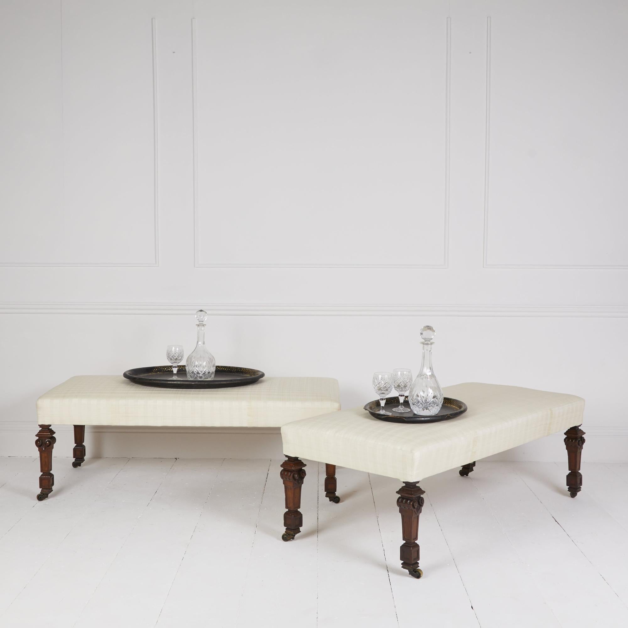 Paire de tabourets de style carrossier traditionnellement rembourrés et recouverts de tissu de crin crème.

reposant sur des pieds et des roulettes en acajou sculpté de style anglais antique Gillows.

Convient comme table basse ou comme siège de