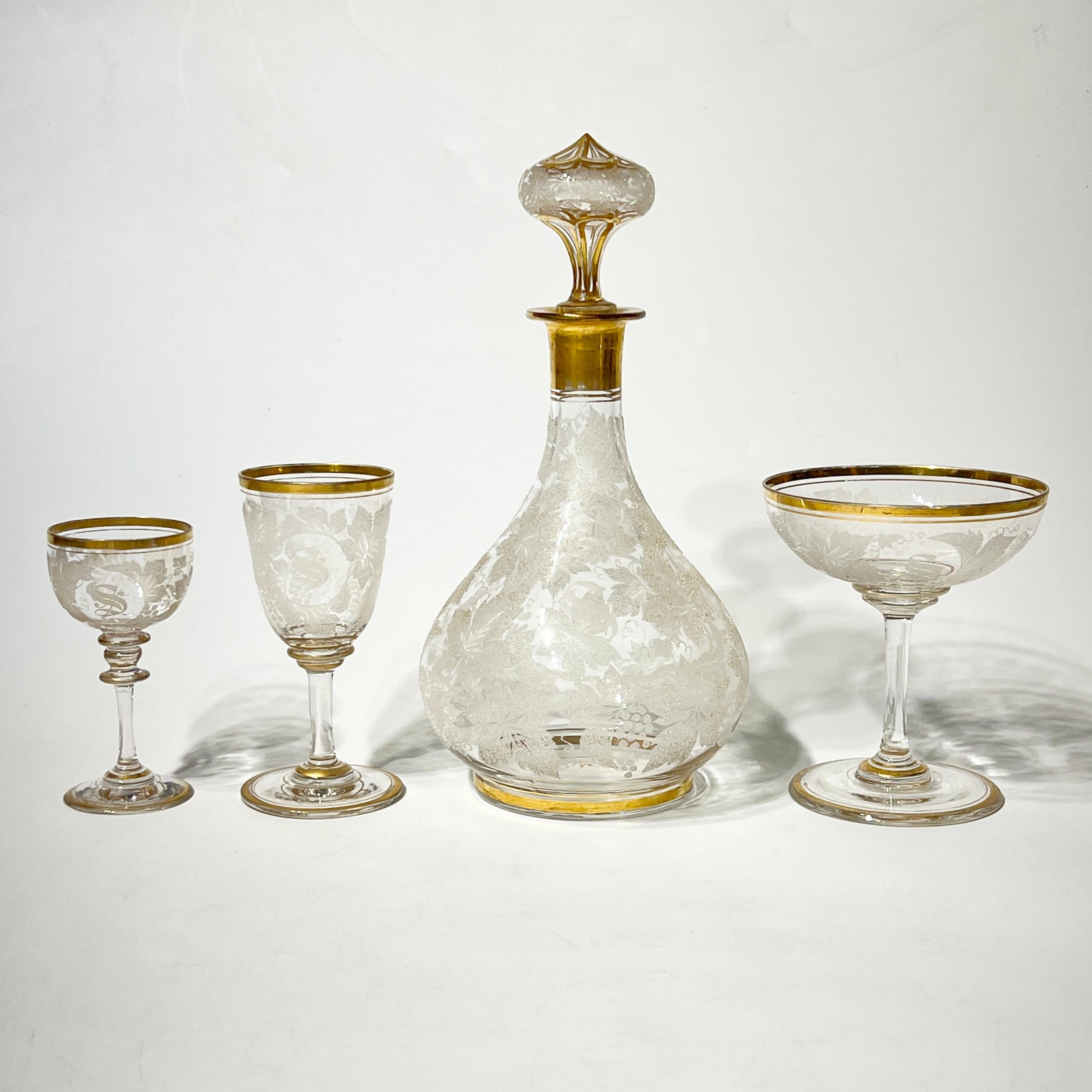 Maravilloso juego antiguo (finales del siglo XIX) de cristalería soplada a mano que incluye dos decantadores, 11 copas de champán, 7 copas de vino y 2 copas de cordial, cada una con finos diseños de vides y hojas en coralina blanca y dorado en la