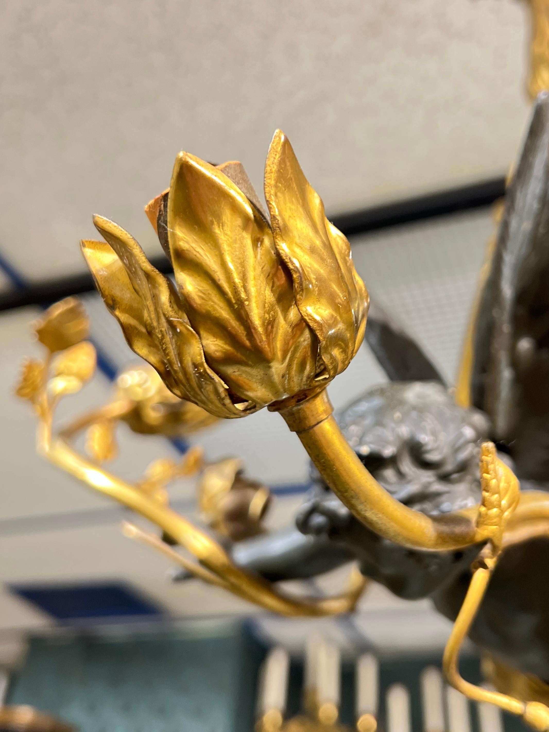 Antique gilt bronze chandelier with three sockets and the patinated figure of Cupid (putto, cherub) in flight inside a foliate form hoop with three sockets.  22 by 18 by 12 inches.