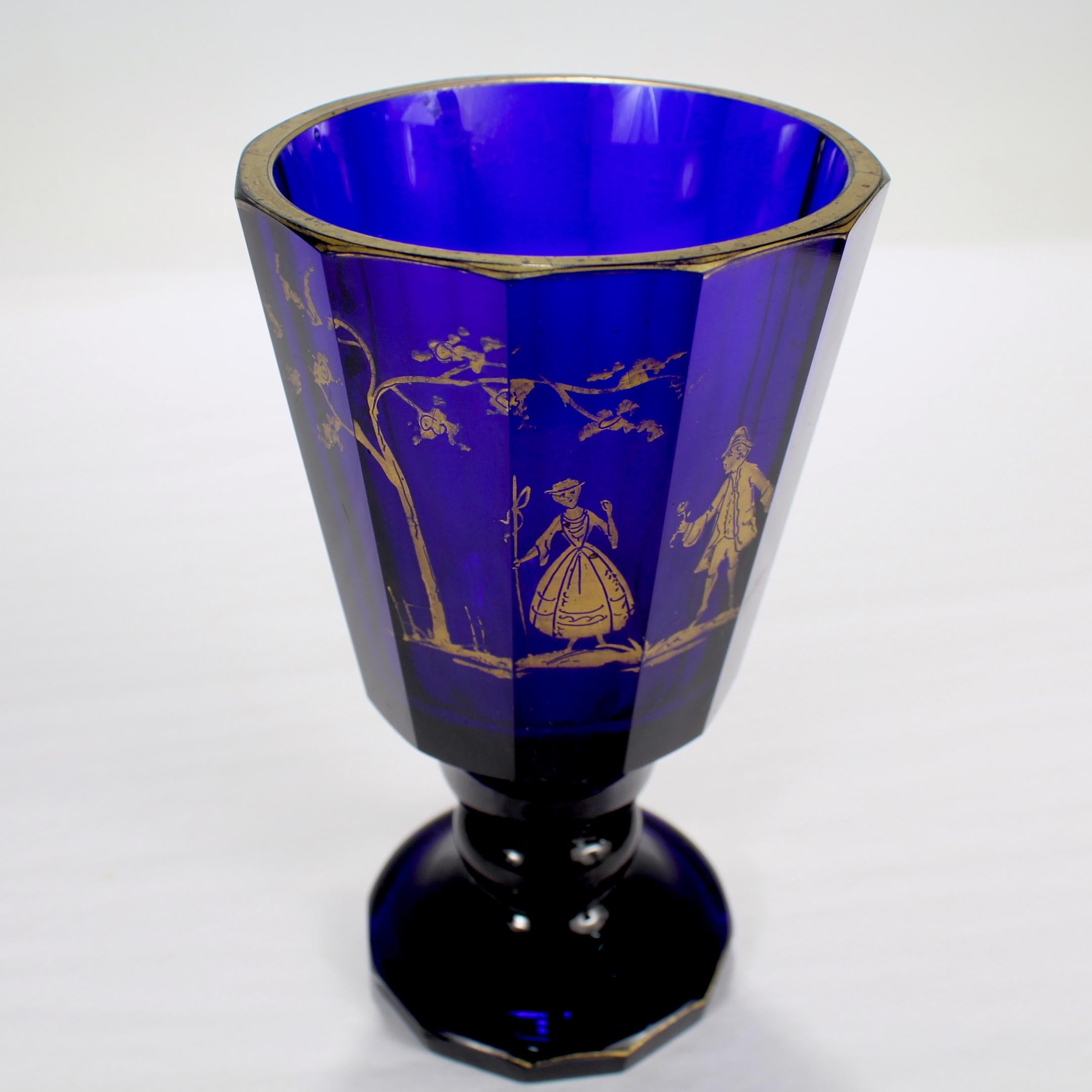 A fine antique Bohemian glass tumbler or beaker. 

Faceted into a dodecagon (12-sided) shape.

The glass has a gilt depiction of a man offering a flower to a woman beneath a tree.

Both the rim and foot are decoratively gilt as well.