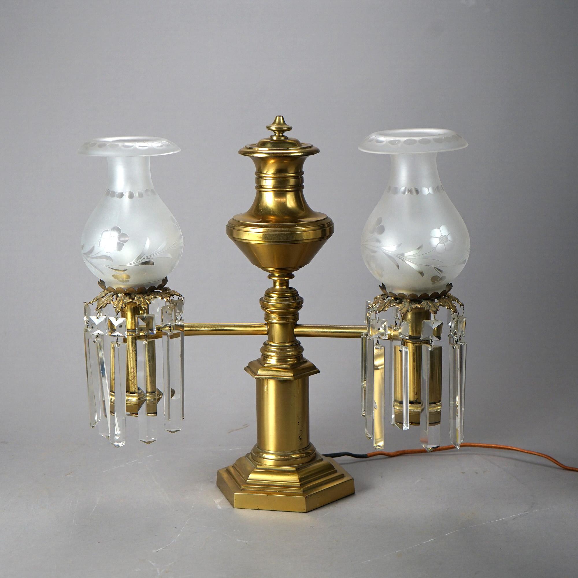 An antique Argand table lamp offers brass and bronze construction with urn form font over double arms terminating in lights having floral etched frosted shades and crystal prisms, raised on plinth with hexagonal base; electrified; 19th