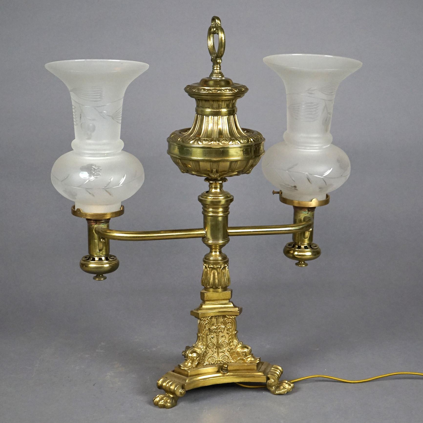 An antique argand lamp offers gilt brass and bronze construction with faceted font surmounting base with double arms terminating in frosted glass shades and raised on foliate embossed base having paw feet; electrified; circa 1820

Measures- 21''H