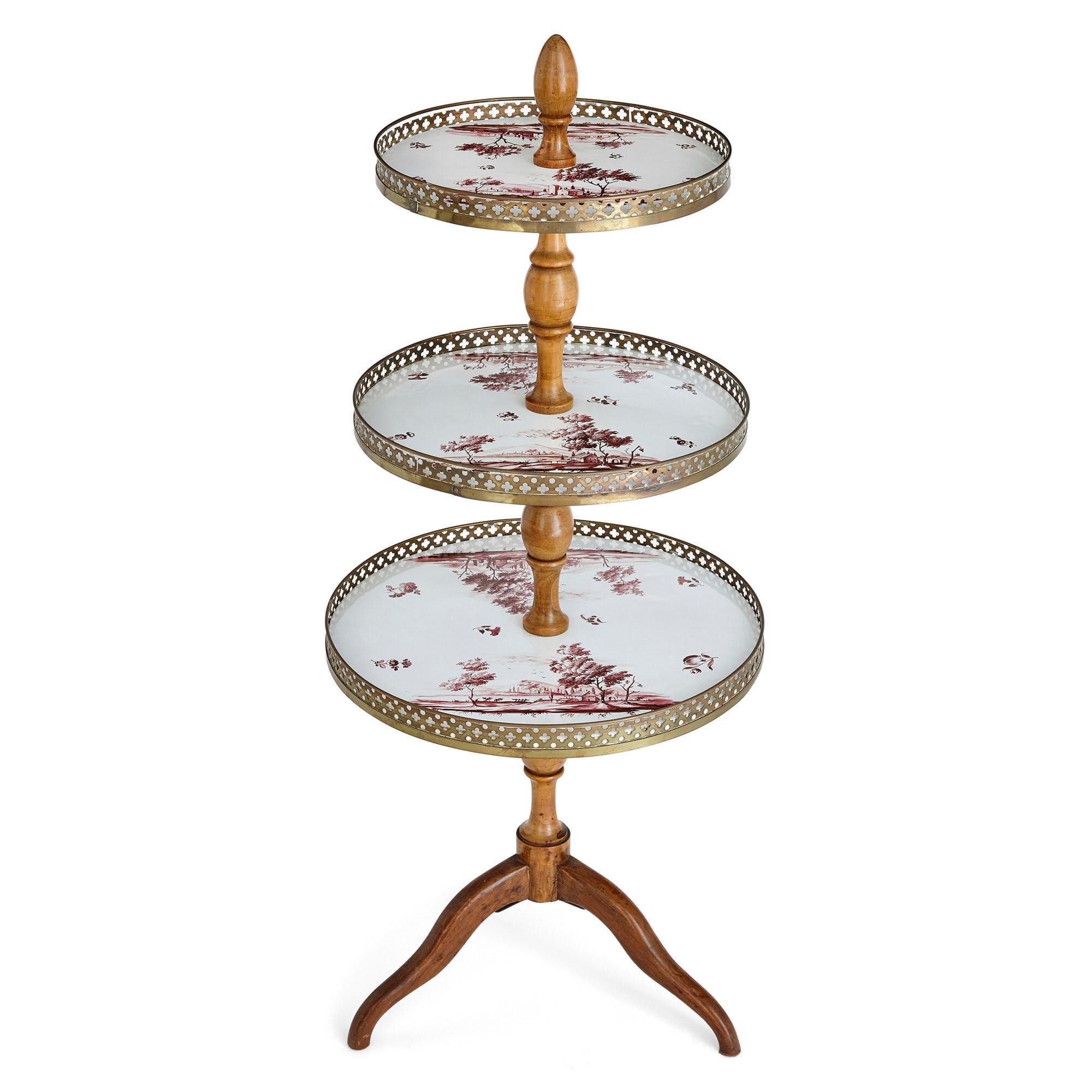 This fine and elegant cake stand features three tiers, each crafted with delicate pierced gilt bronze galleries and porcelain bases, with landscape scenes painted in red pigment on white ground. The tiers are supported by a central beechwood stand,