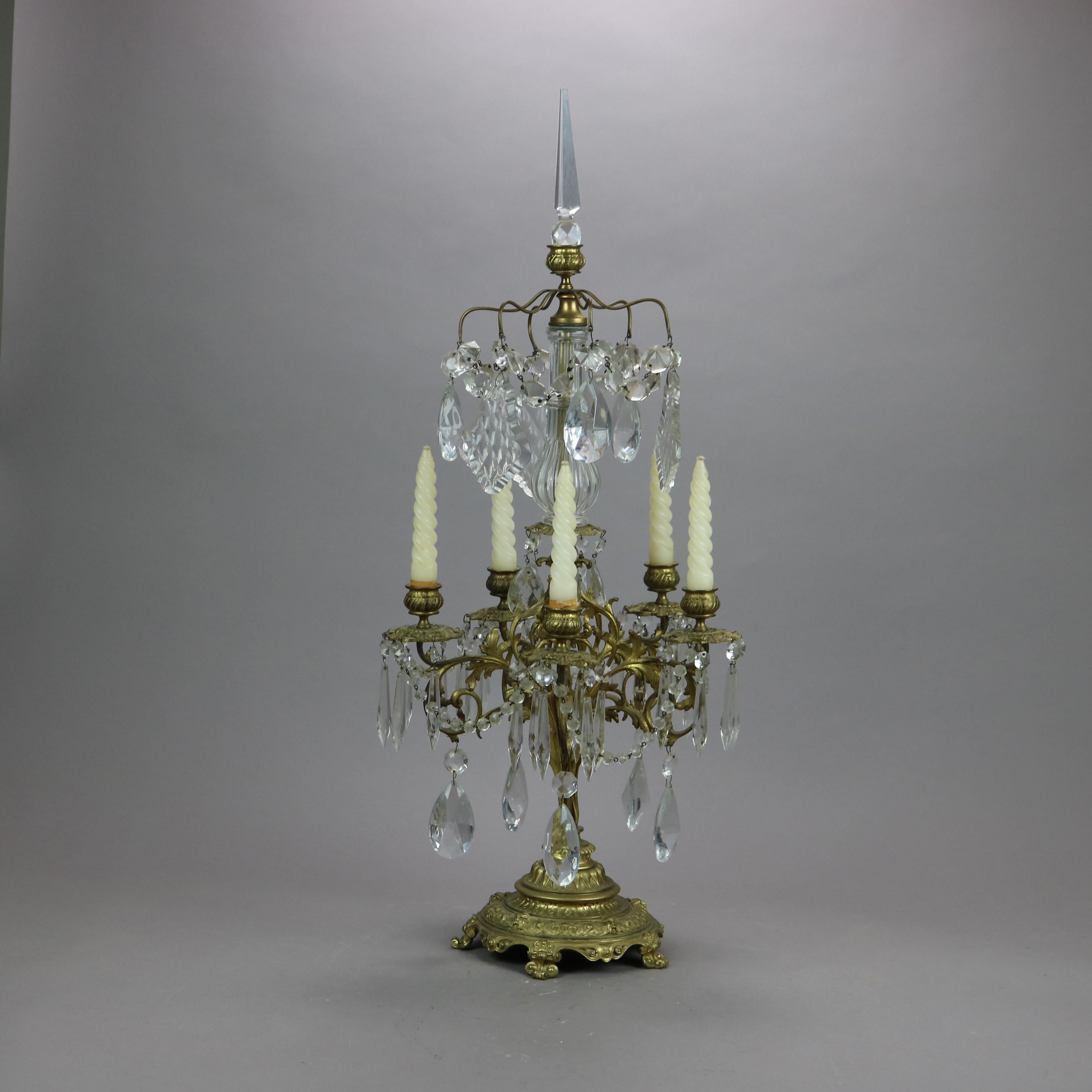 An antique Victorian candelabra offers gilt cast bronze construction with crystal spire surmounting base having five foliate scrolled arms terminating in melon ribbed candle sockets, raised on footed base, cut crystal prisms throughout,