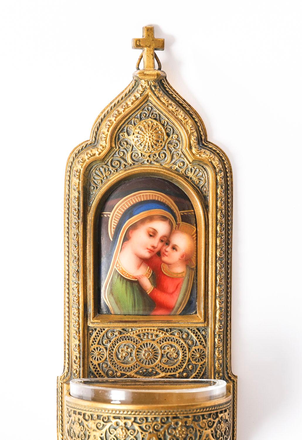 This is a beautiful 19th century gilt bronze wall hanging holy water stoop in Gothic revival style.

The ormolu font with a cross pediment and a superb arched enamel panel depicting the Virgin and child above a cut crystal demilune bowl for the holy