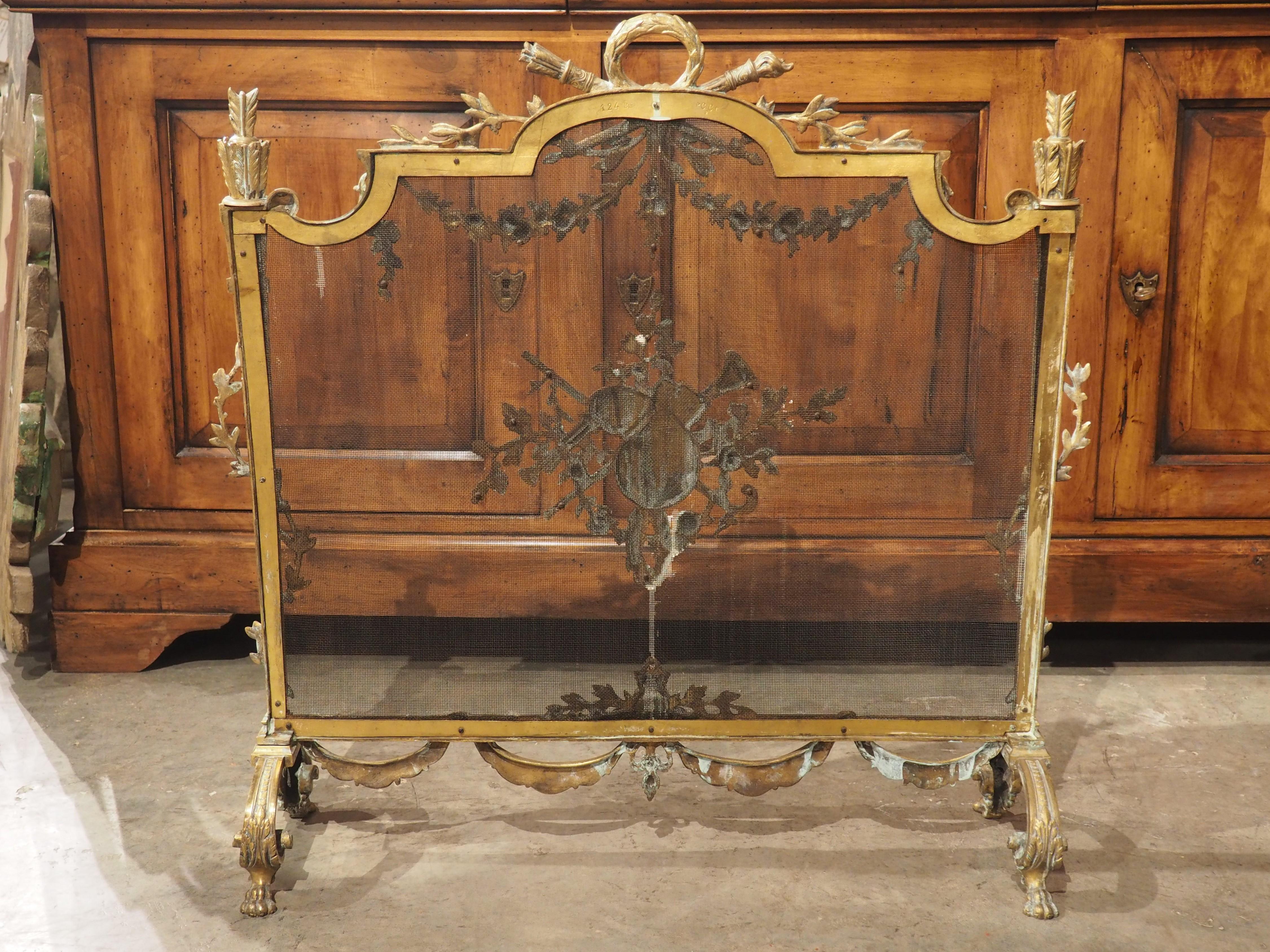 Hand-crafted in France, circa 1880, this gilt bronze firescreen is embellished with Louis XVI-style motifs. A very fine iron mesh is surrounded by a bronze frame set on two high arching legs adorned with imbricated disks, volute leaves, and a pair