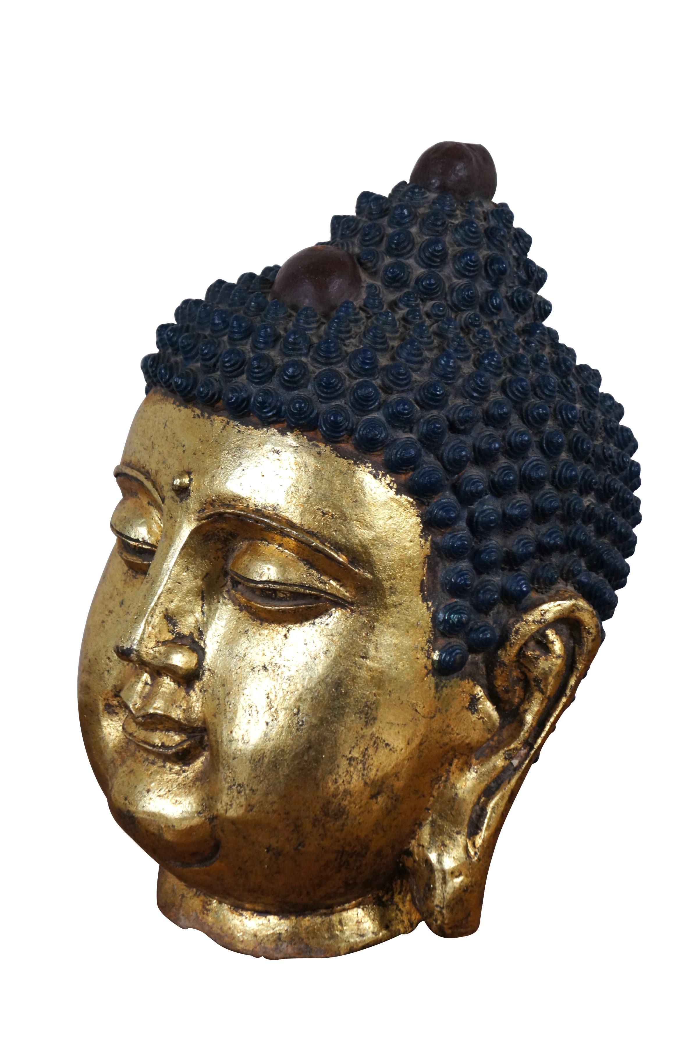 Antigua cabeza de Buda meditabundo de hierro fundido. De hierro, con cara redonda, lóbulos de las orejas alargados y bindi en el centro de la frente, piel pintada de dorado brillante y tirabuzones de pelo rizado de color azul intenso con dos piezas