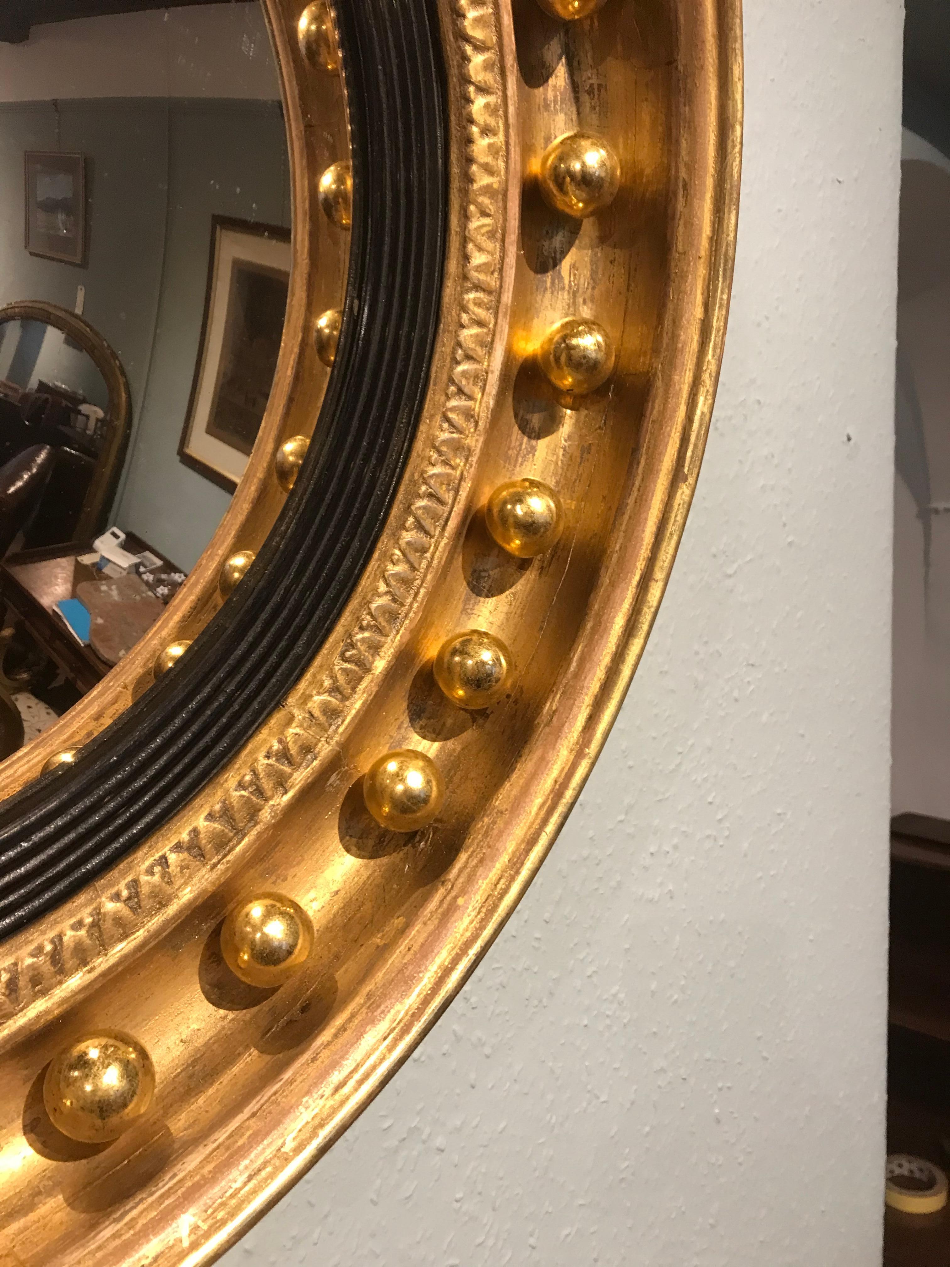 Stunning gilt convex mirror circa 1850. The mirror features a concave frame, decorated water gilded spheres, inset with an ebony reeded slip. The mirror plate is original, ornate carved scroll and leaf decoration to the top.