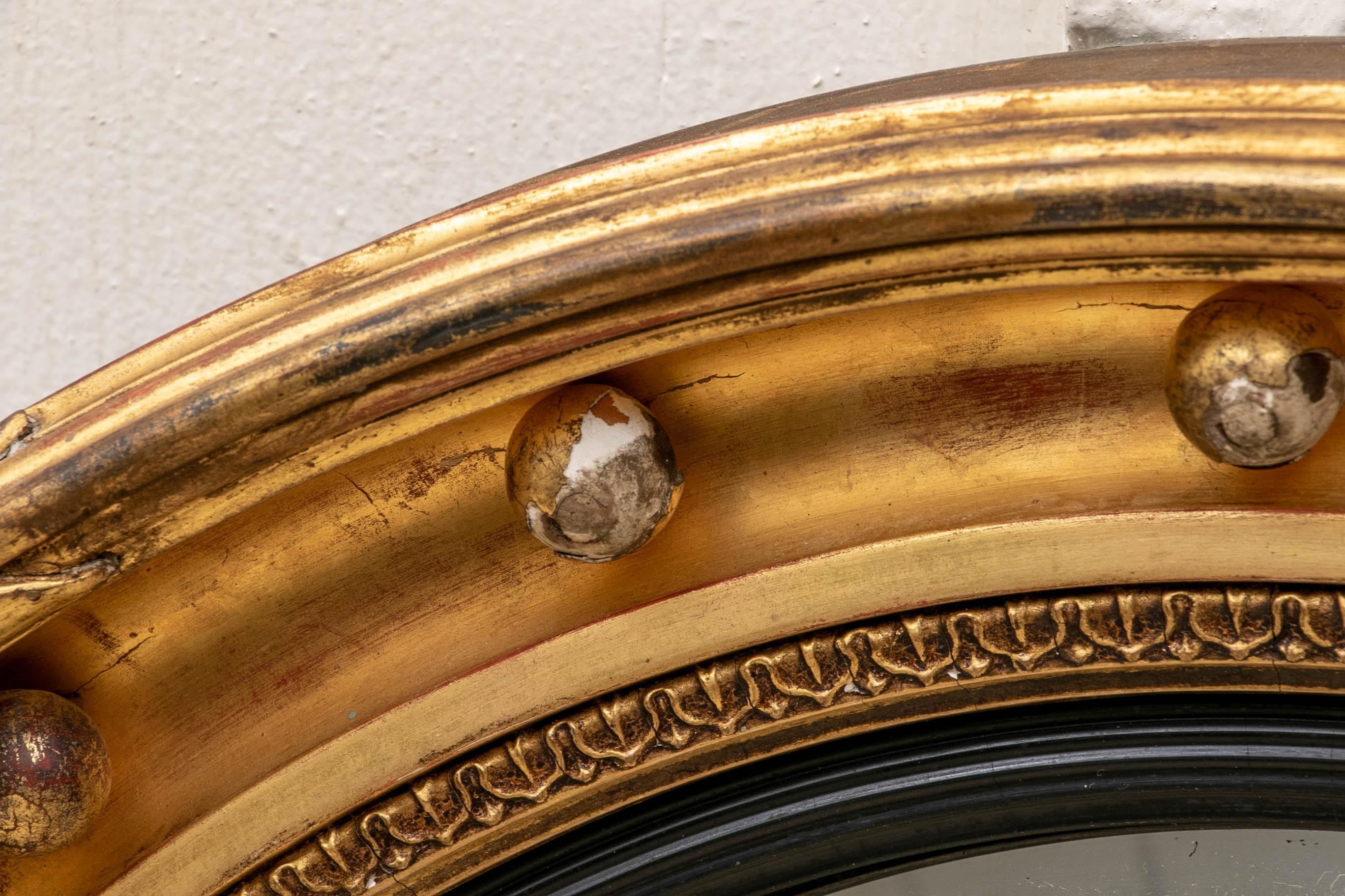 Antique gilt framed convex mirror, reeded outer surround with ribbon details, a middle one with spheres, an inner leafy band, and a reeded ebonized innermost surround.

Condition: Good condition with expected signs of use including some expected