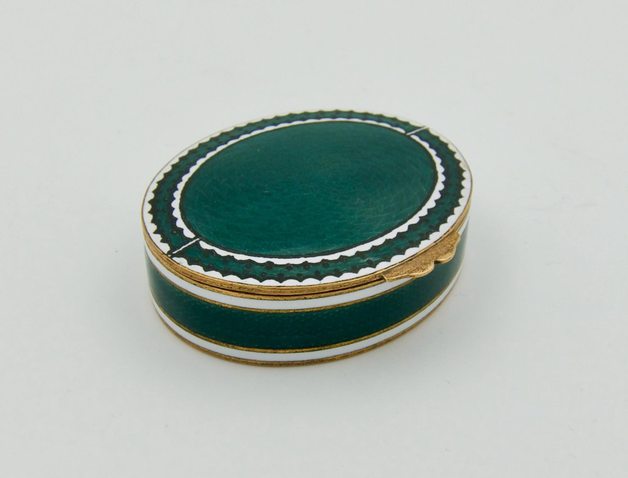 An antique snuff or pill box in gilt metal with guilloche enamel decoration in green, black, and white. The hinged box of elliptical form is raised by a simple thumb piece. The lid is decorated with a field of dark green enamel over an engine-turned