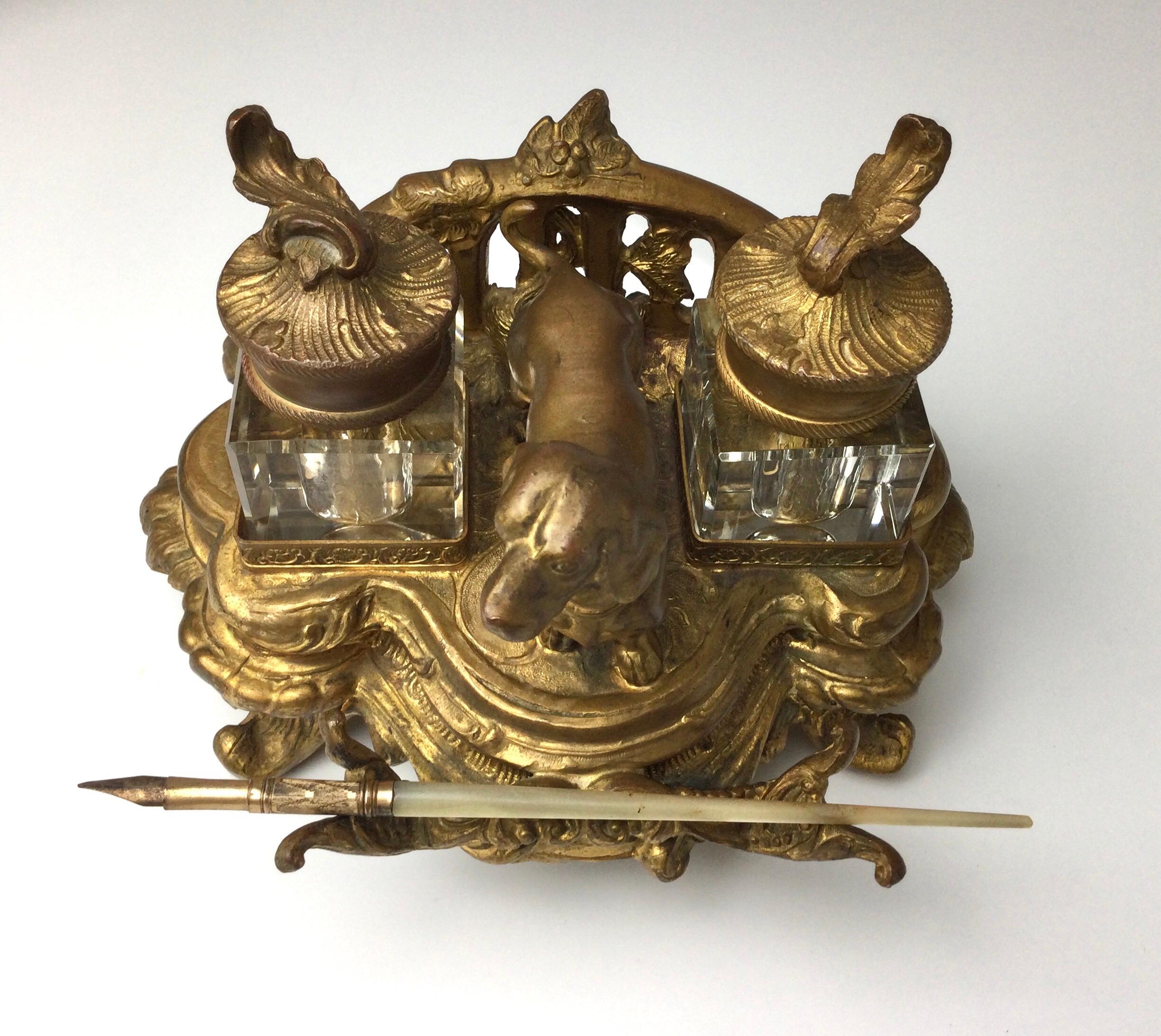 Antique gilt metal double glass inkwells with dachshund dog in nice age appropriate condition. The gilt has a nice patina, late 1800s. Measures: 6 1/2” wide by 4 1/2” deep by 4 1/2” to top of finial. Glass inkwells are removable with no chips or