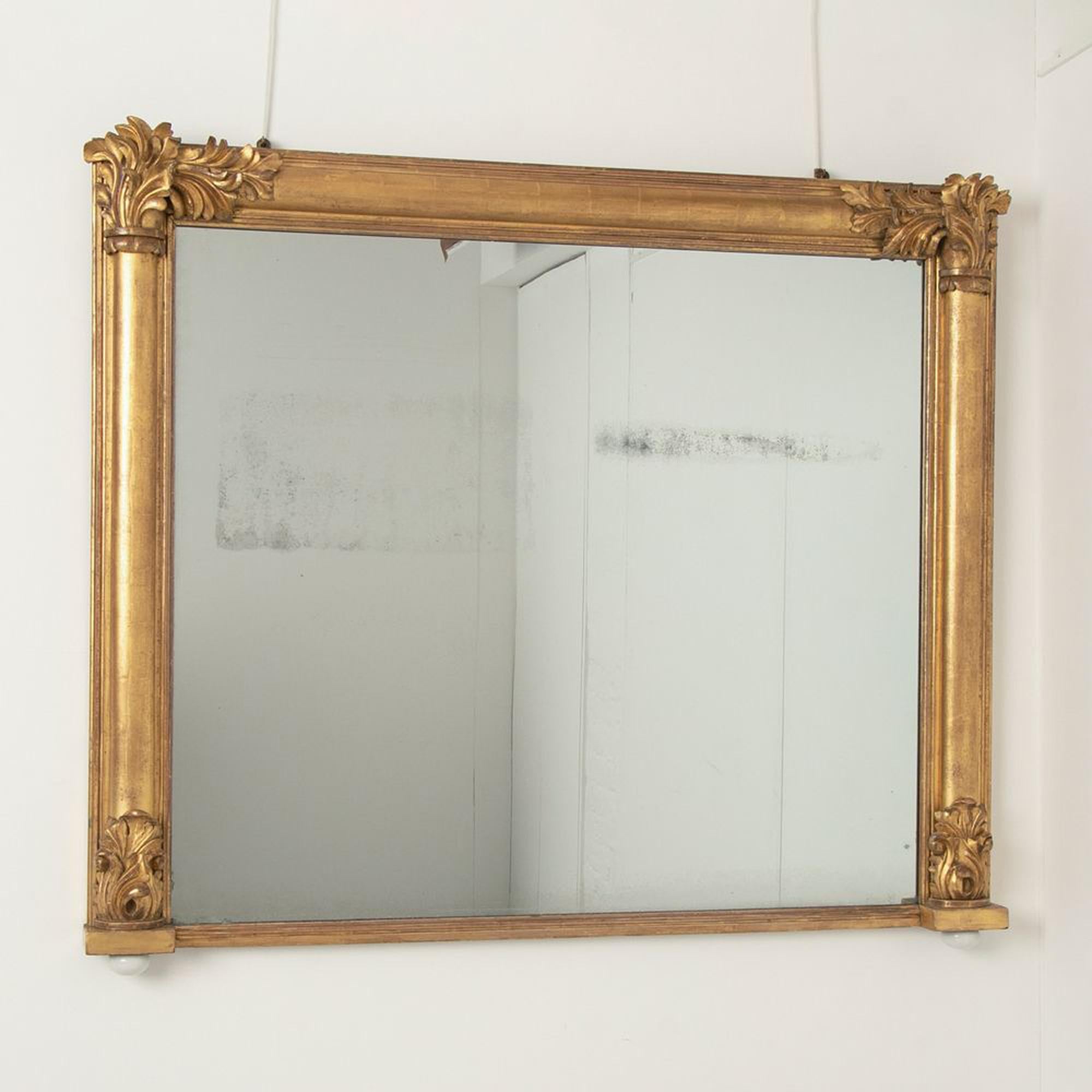 An antique gilt overmantle mirror by Willian Cribs, rectangle in shape with carved leaf details on each corner. The mirror retains its original mercury silvered mirror plate and original water gilding. There is foxing to the glass.