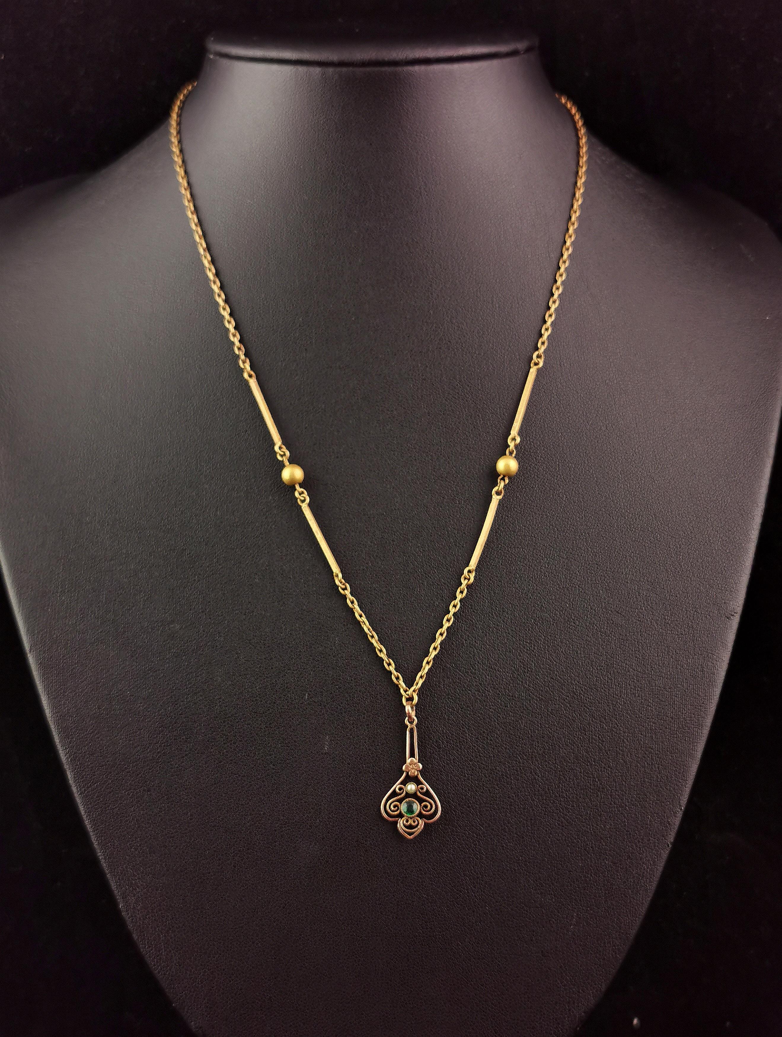 A beautiful antique, Edwardian era pendant necklace.

The chain is a rolo link chain in gilt plated brass, the chain intercepted with fancy bar and ball links.

It has a small gilt metal pendant suspended, an openwork design set with a rich green