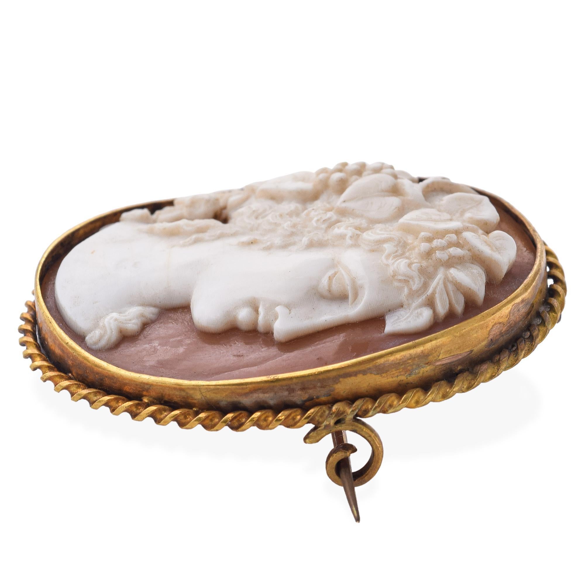 This antique shell cameo brooch features a finely carved portrait of Bacchus, the Roman god of wine, revelry, and ecstasy. He is shown crowned with grapevines, a classic symbol of abundance and festivity. Set in a warm gilt metal frame, the piece