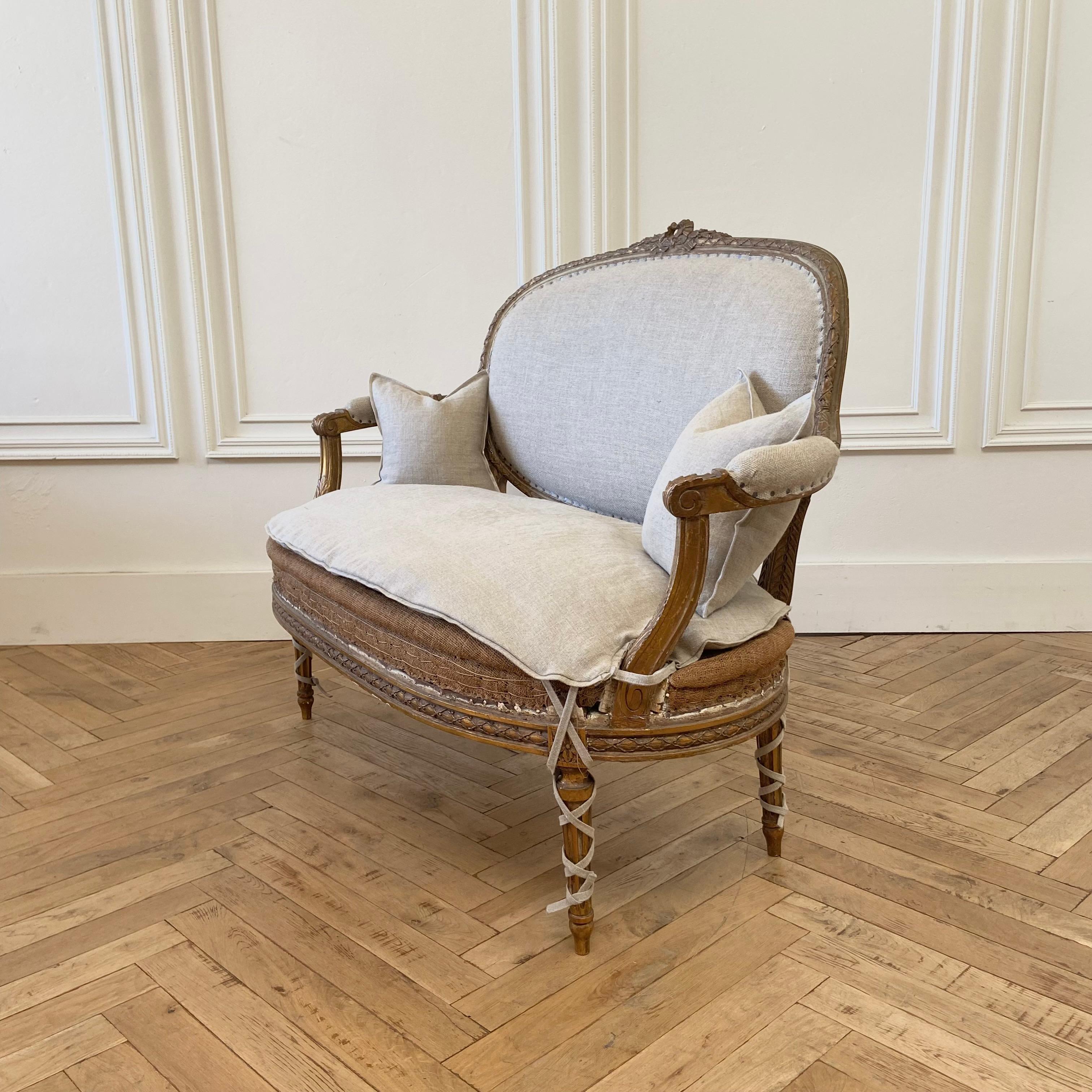 Antique gilt wood French Louis XVI style open arm settee
Lovely with its original gilt wood patina finish, fading gilt rubbed through with exposed bole, a classic
ribbon carving, and fluted column legs.
We have reupholstered this in our 100% pure