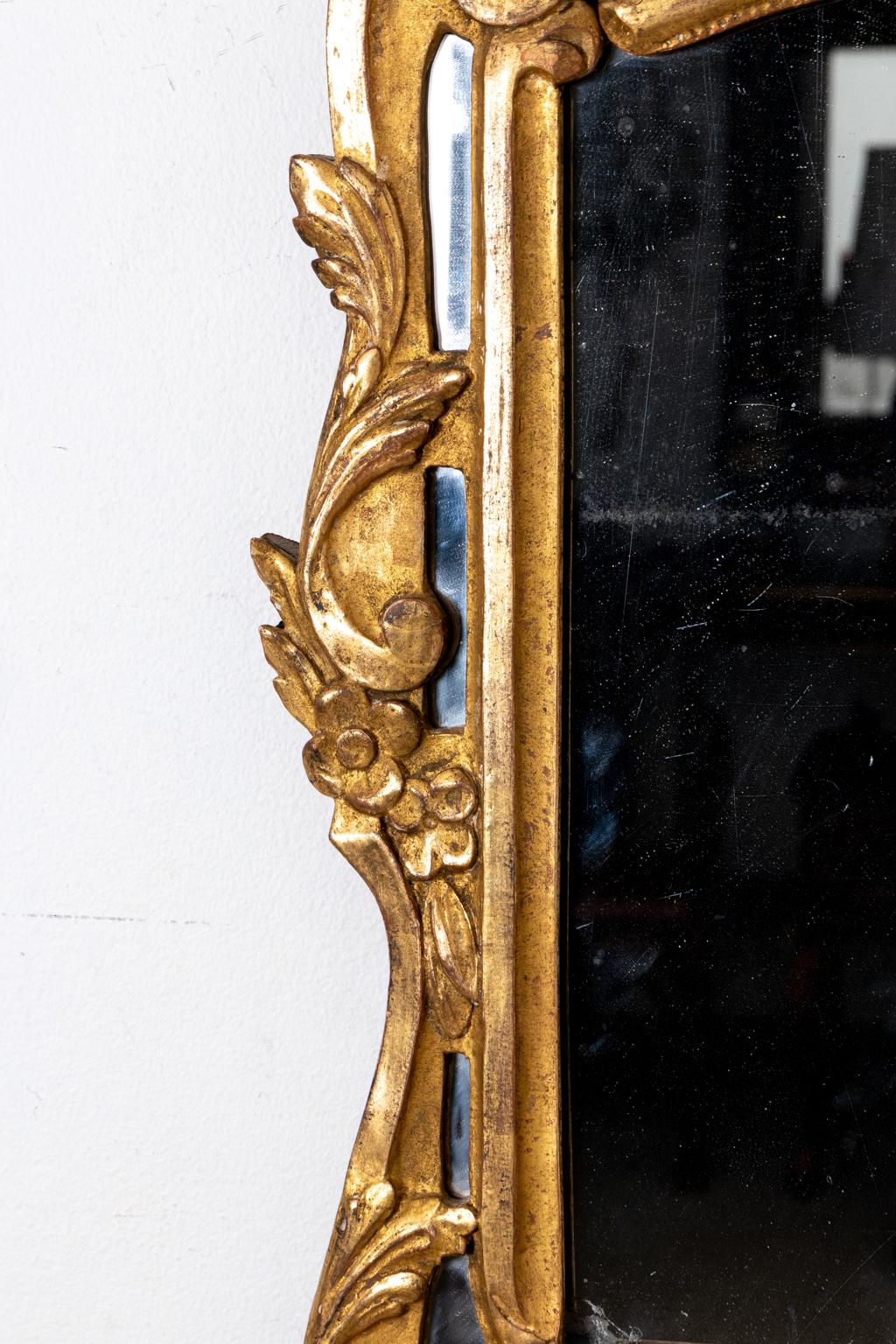 Circa 1890s antique giltwood mirror with dark accent paint, ornate crown, c-scrolls, and floral motifs surrounding the frame. The crown features three plumes of feathers on top of a carved medieval style helmet with draped floral swags framing a