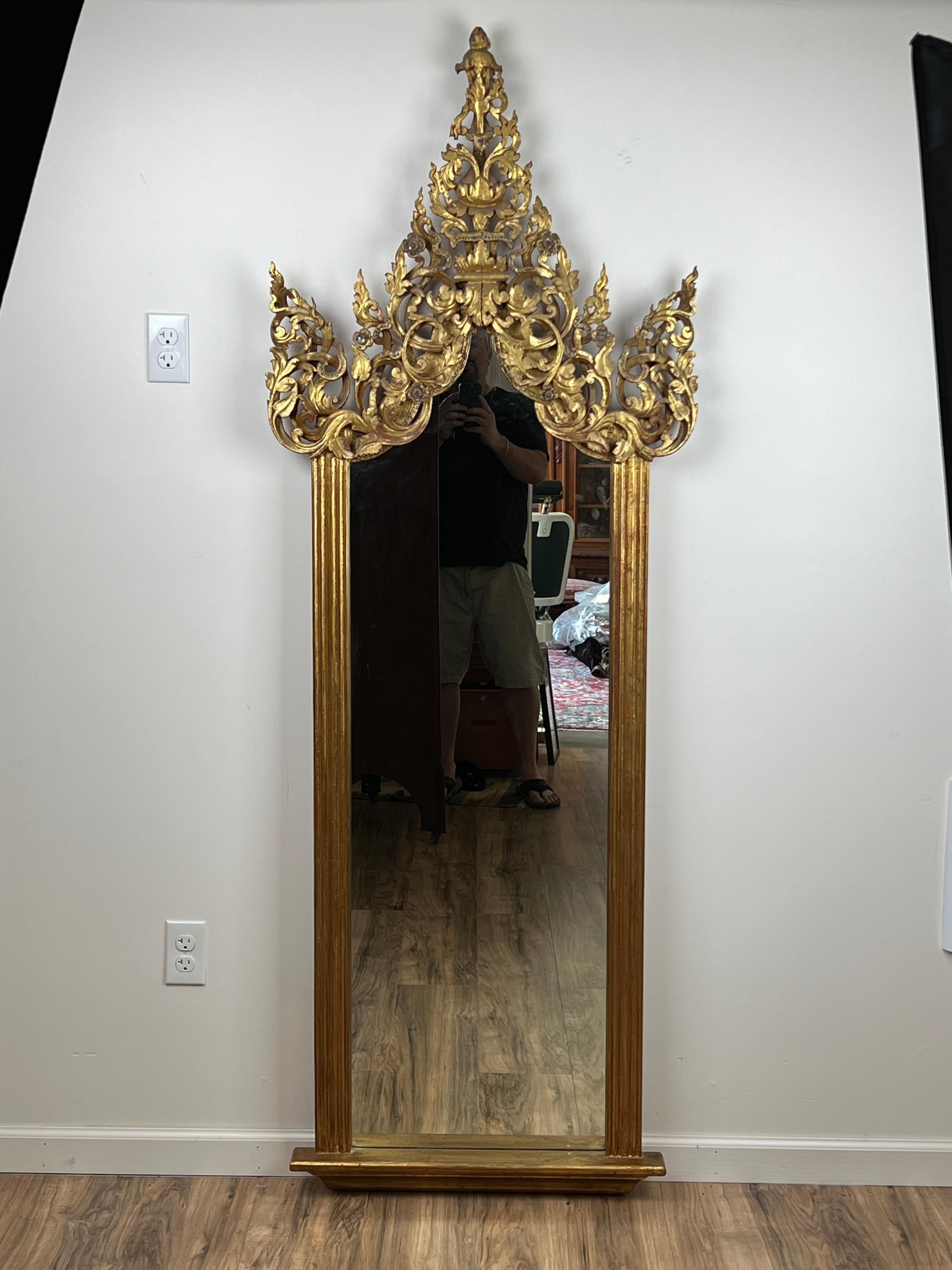 Este Antiguo Espejo de Santuario birmano de madera dorada, del siglo XIX, muestra la intrincada artesanía característica del rico patrimonio artístico de la región. El marco está adornado con una corona de madera dorada muy detallada, con elementos