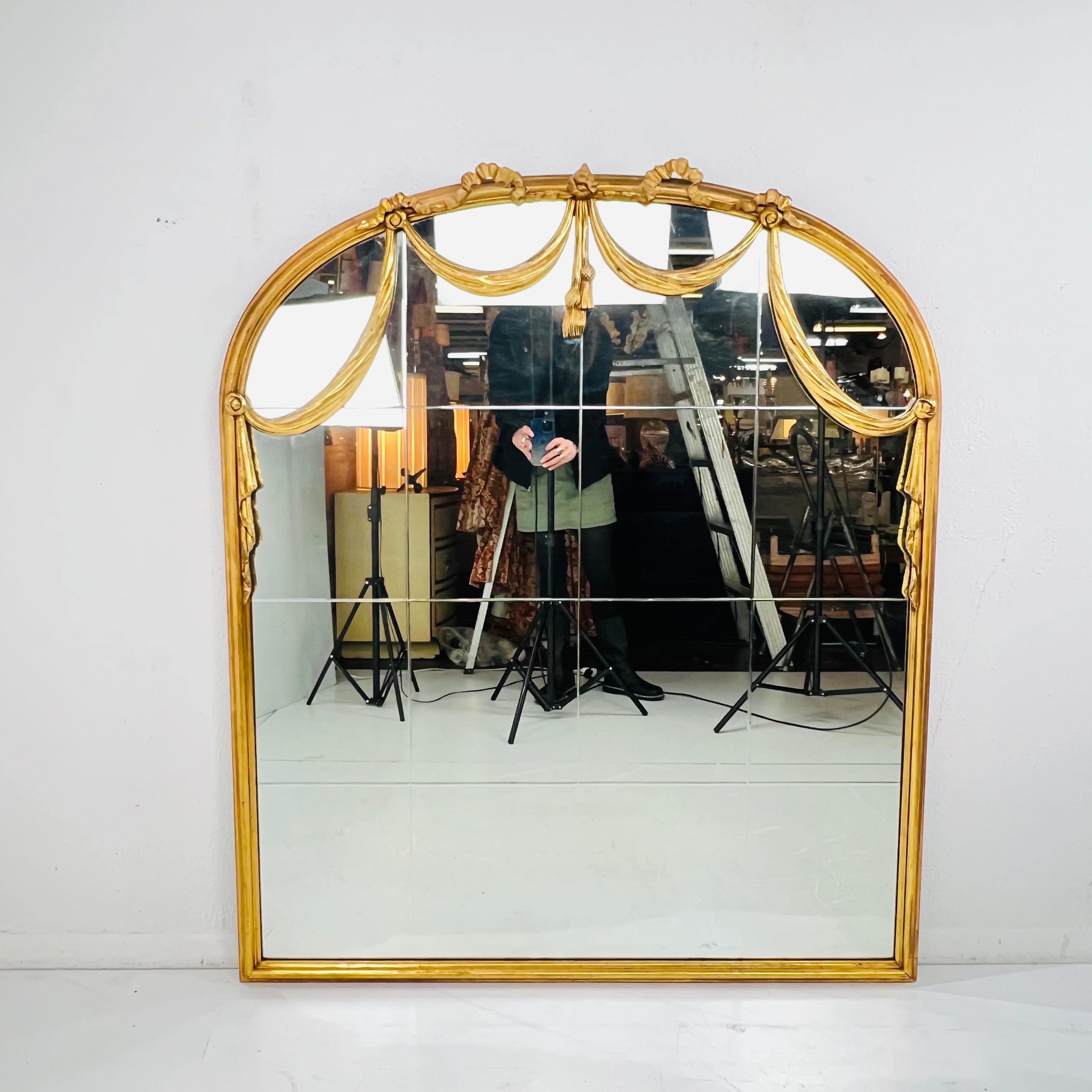Miroir mural ancien en bois doré avec deux draperies sculptées et un sommet en forme d'arche avec des glands. Le miroir a des vitres gravées. Bon état vintage avec une usure normale due à l'âge et à l'utilisation, pas de cassures ou de fissures sur