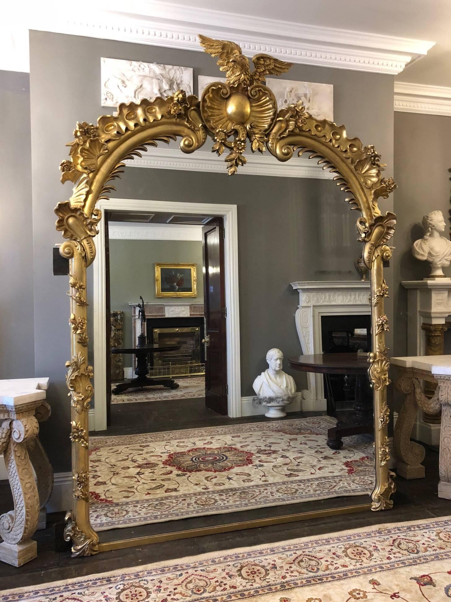 Un miroir en bois doré sculpté de très grande échelle et de grande qualité, fabriqué par Froom & Cribbs de Londres. Le cadre en bois magnifiquement sculpté est décoré de fleurs et de feuillages. Le sommet arqué à volutes est centré par un cartouche