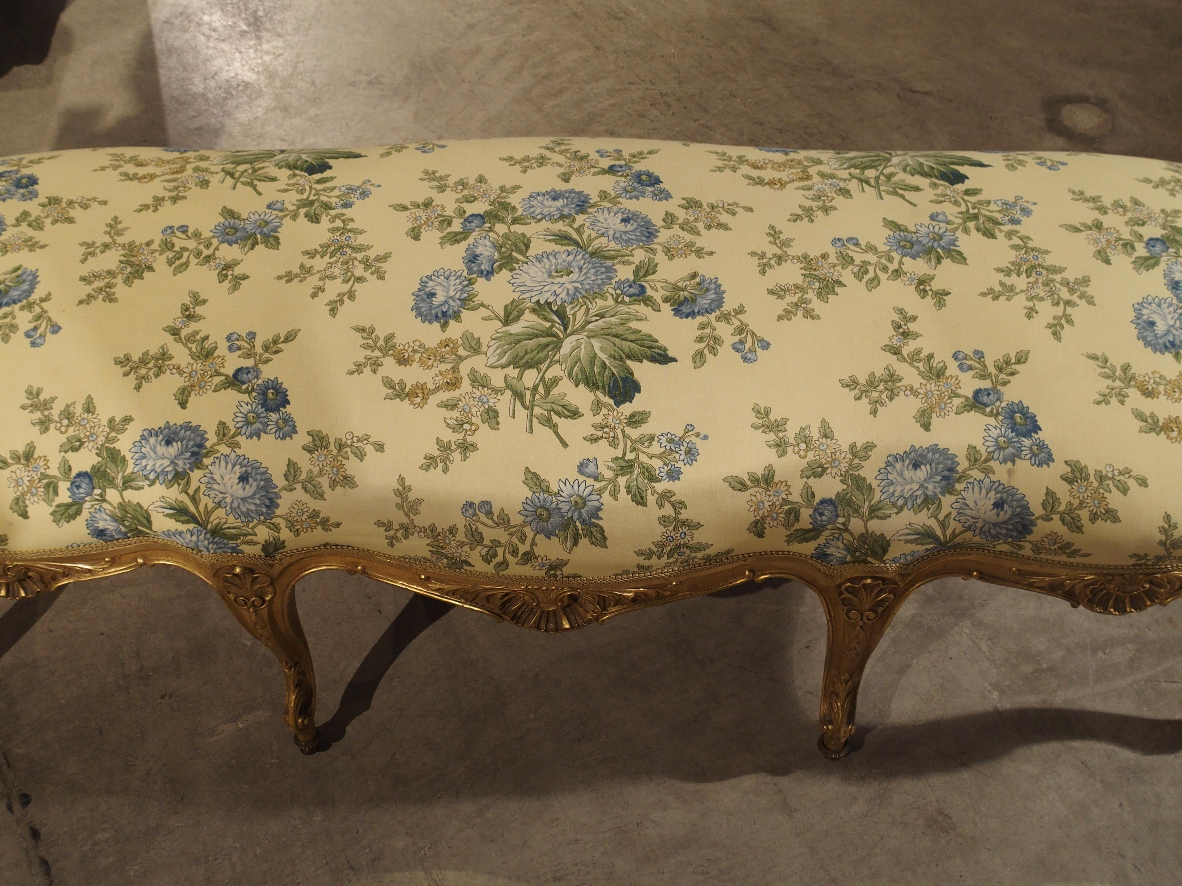 This stunning gilded, eight leg, antique French Regence style banquette dates to the 19th century. It has been reupholstered in a fabric with a pale yellow ground having stems of large pale blue Chrysanthemums and smaller stems of pale blue