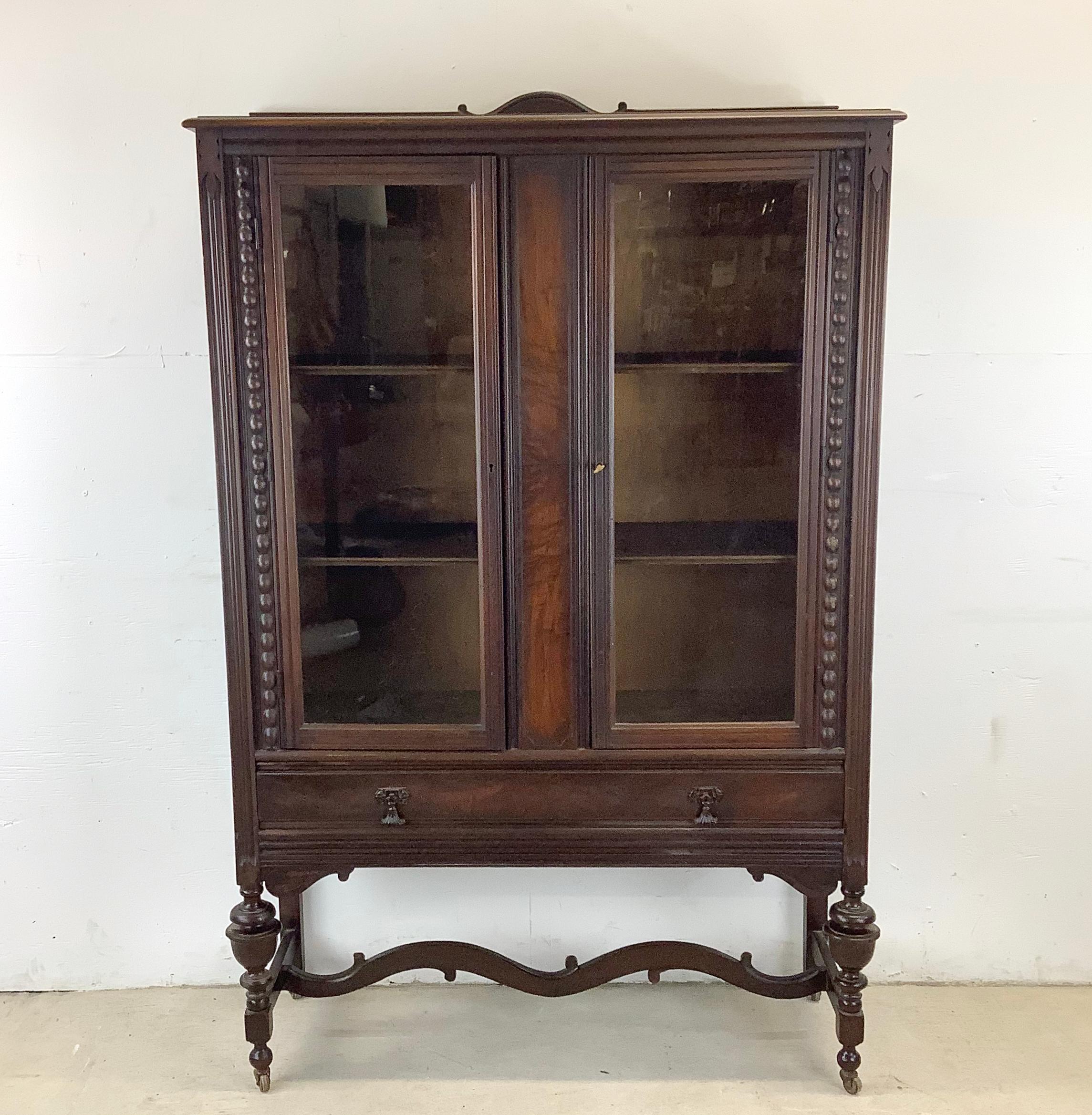 Introducing this Antique Carved Wood Glass Door Bookcase With Sculptural Stretcher -  a stunning piece of history that adds both elegance and functionality to any home. Crafted with exquisite attention to detail and featuring beautiful glass doors,
