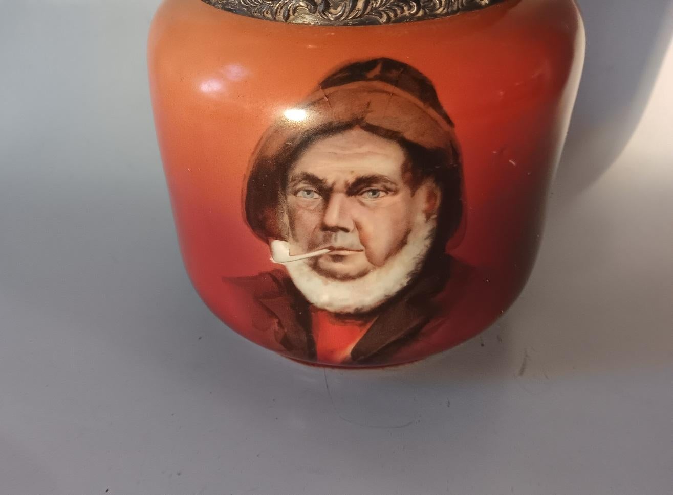 Antique early 20th century milk glass and silverplate humidor or cigar jar.  Painted exterior in orange and terra cotta with transferware image of a bearded sailor smoking a pipe.  Silver plated lid and rim, dark patina, with some scuffing and one