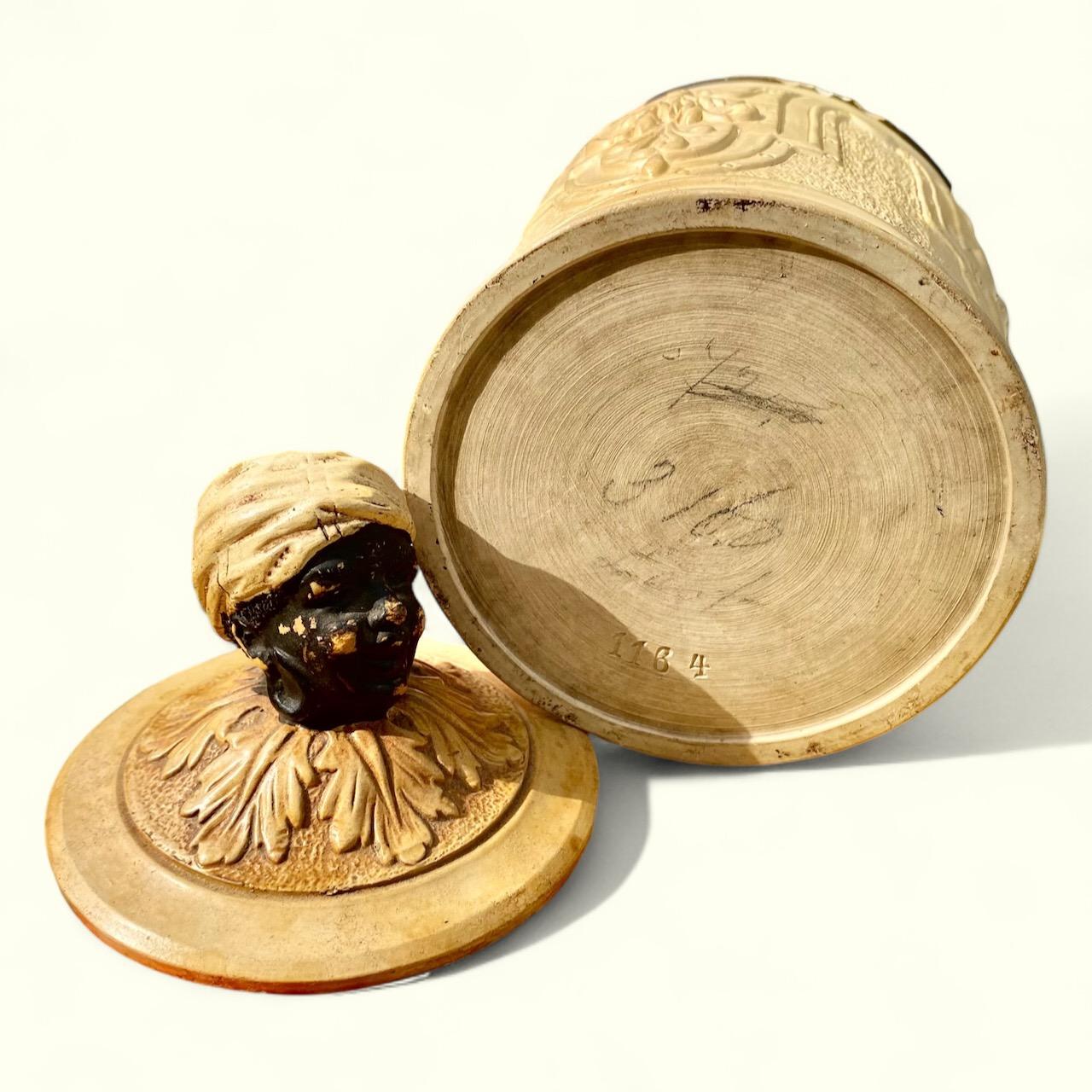 Un bel humidificateur ancien en forme de Blackamoor coiffé d'un turban et dont le couvercle est orné de feuilles en volutes. La base présente des armoiries détaillées et stylisées ainsi qu'une belle texture. Entièrement créée et peinte à la main par