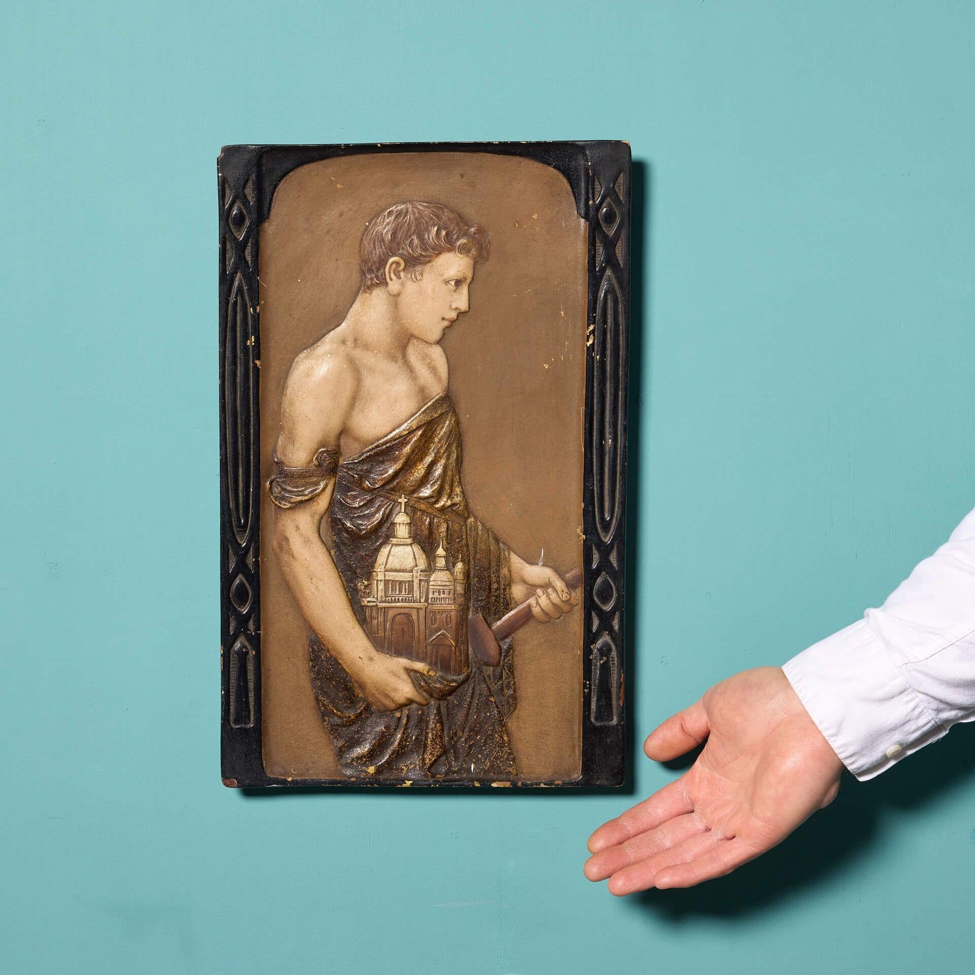 An antique glazed terracotta panel depicting an architect holding his masterpiece. This impressive panel displays detail and lustre making it a striking piece for any property. A domed church sits in the hand of the Roman man dressed in drapes,