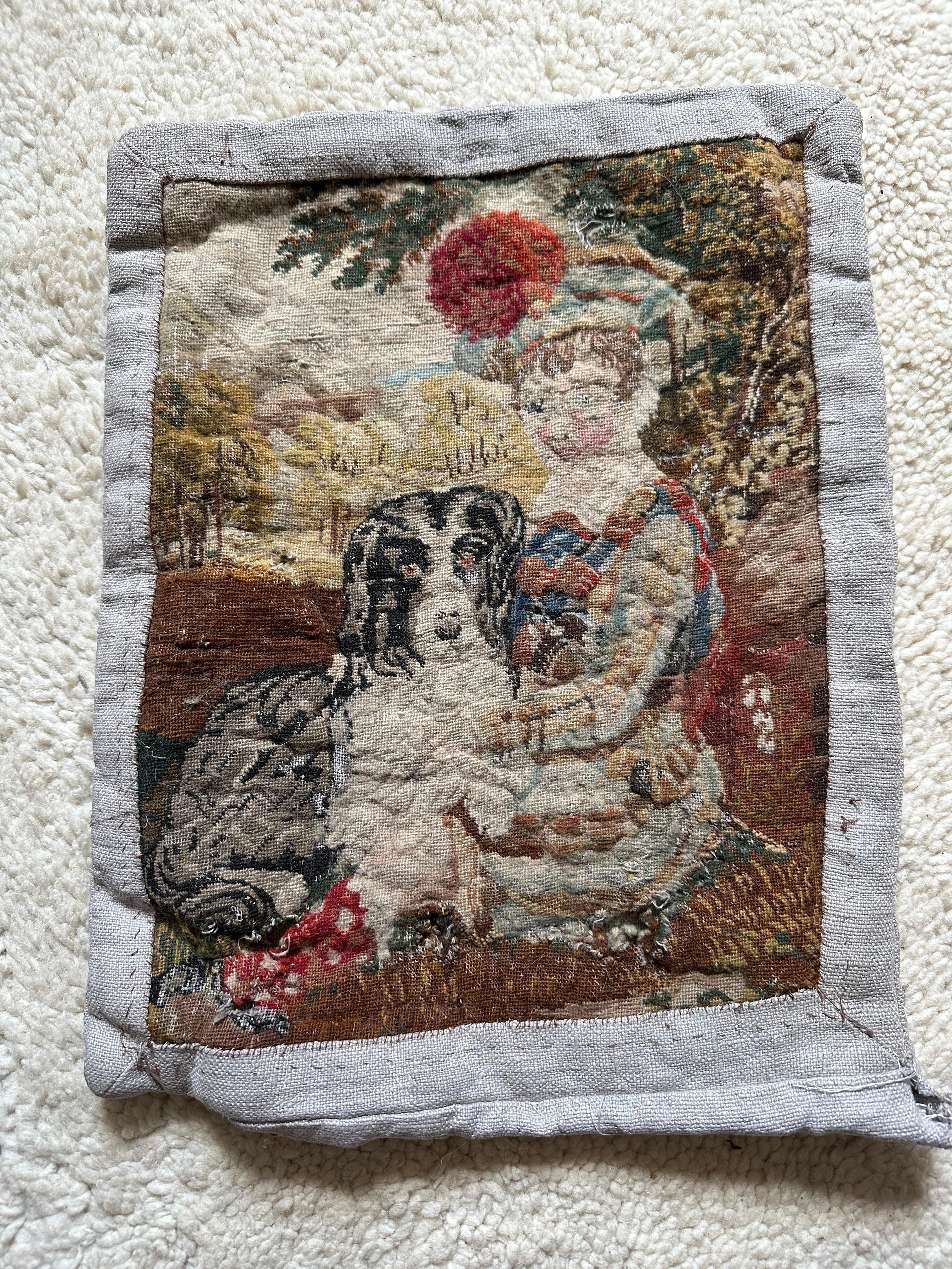 Sumérgete en el encanto del siglo XVIII con este exquisito cojín antiguo, elaborado a partir de un fragmento de un tapiz gobelino histórico. Esta pieza única muestra una encantadora escena de un niño con su perro, intrincadamente tejida y llena de