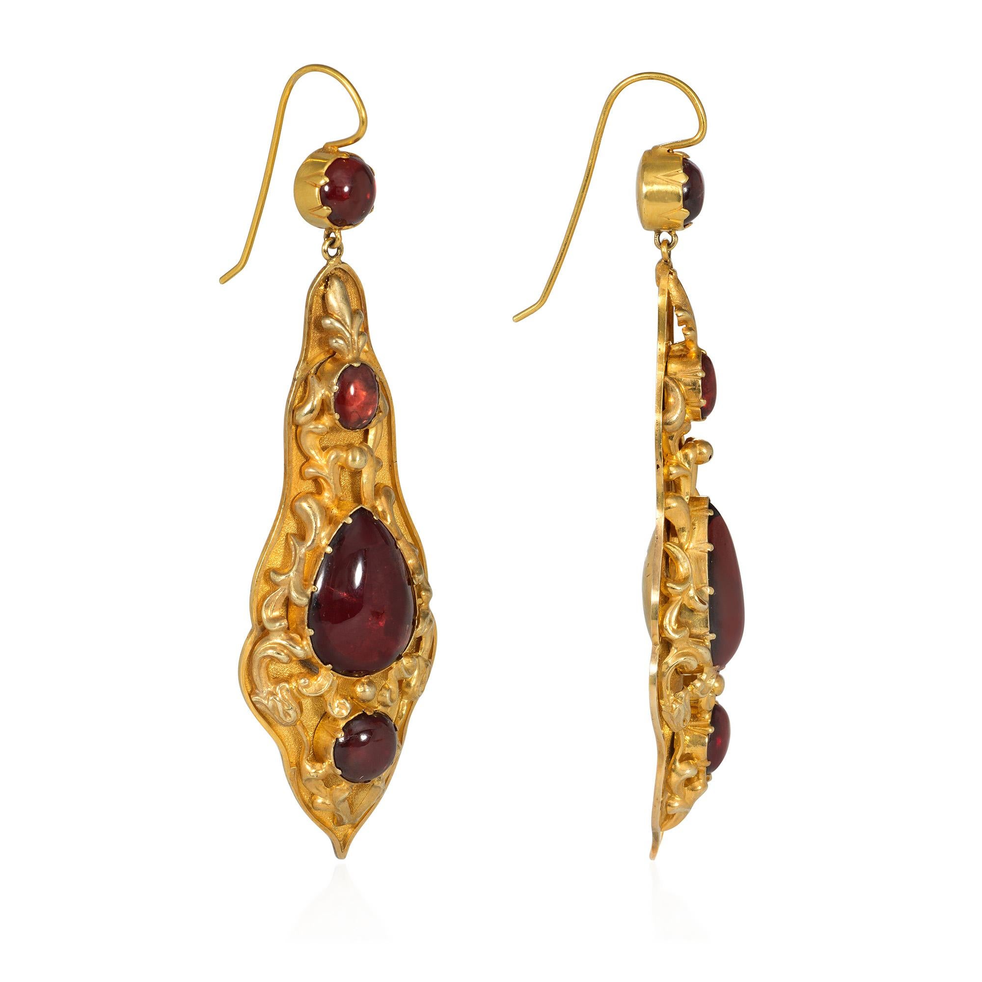 A pair of antique Georgian period gold and close-backed garnet earrings, the long pendants of tapering design and set with oval, pear, and round cabochon garnets surrounded by applied gold repoussé decoration, suspending from round cabochon garnet