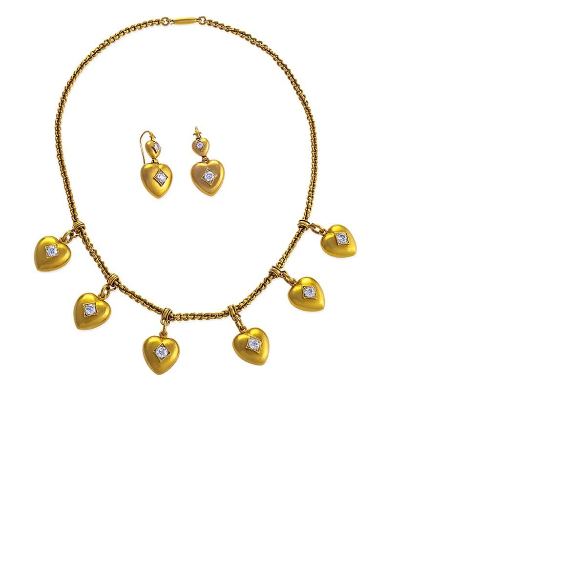 A charming 18 karat gold chain featuring six heart-shaped, diamond-studded dangling charms with a matching pair of two-tiered diamond and gold heart shaped earrings. Each heart in this traditionally sentimental late Victorian suite is studded with