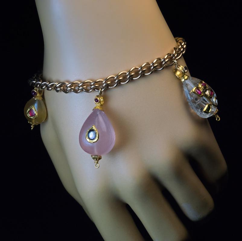 A late 19th century 14K gold link bracelet of a European origin is embellished with five Mughal Indian jeweled charms. The carved hardstone charms are mounted in high karat (22-24 Kt) gold and set with gems: two pink quartz with cabochon cut white