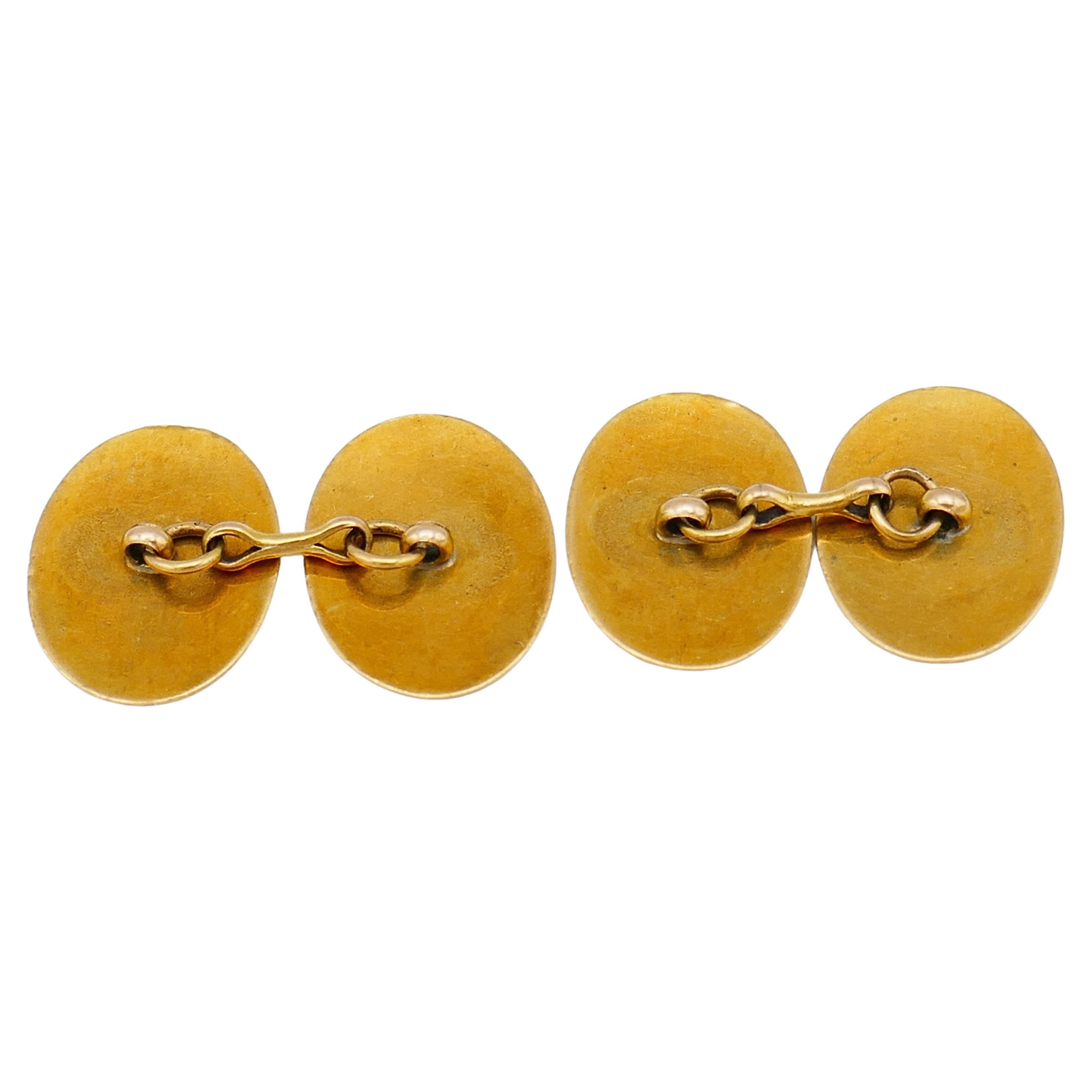 A pair of beautiful antique 18k gold and enamel cufflinks. 
The cufflinks are oval shape, with floral engraving on the edges. One of the cufflinks has an enamel family crest that looks like a stylized fleur-di-lis symbol. Another one has a symbol of