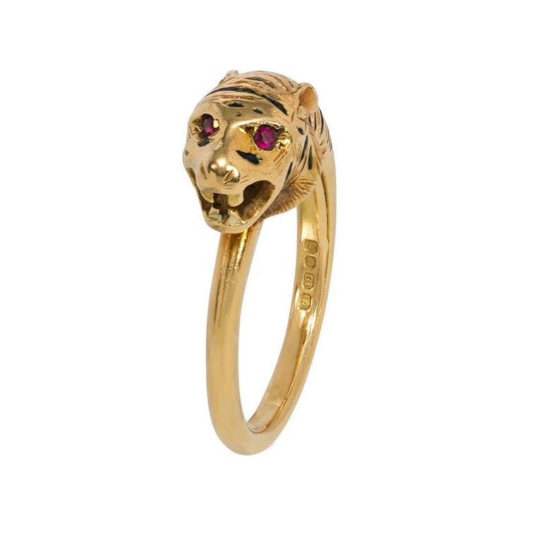 An antique early 20th century engraved gold, enamel, and ruby ring in the form of a tiger, featuring an engraved coat with black enamel stripes, and the eyes set with rubies, in 18k.  England, stamped 