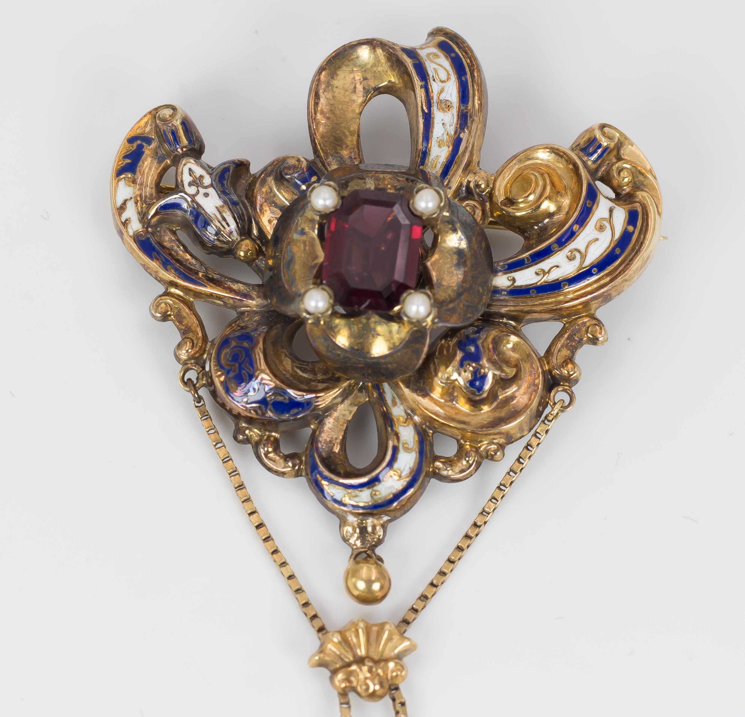 A very elegant antique brooch, dating from the Second Half of the 19th Century, set with a central garnet and four beads; they are surrounded by a gold setting, decorated with white and blue enamels; a gold pendant gives a pretty movement to this