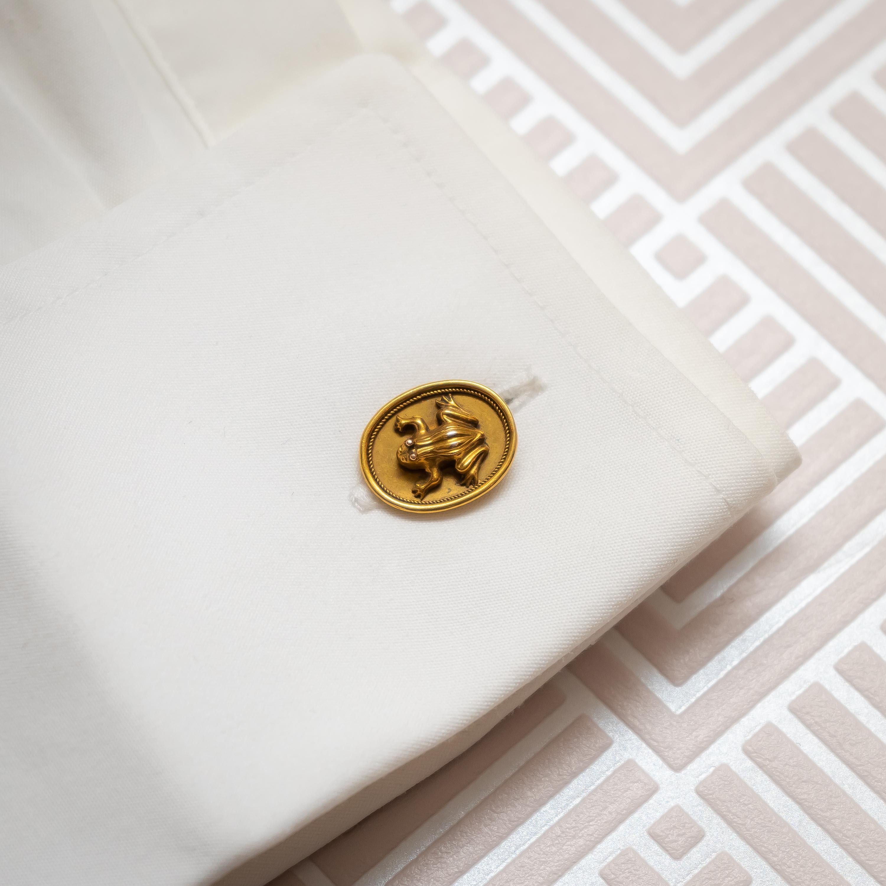 Une paire de boutons de manchette anciens en or, avec des modèles de grenouilles sur des plaques ovales, avec une torsion en fil de fer dans le cadre, montés en or avec une marque numérotée, et des ferrures de barre torsadées. Circa 1900.