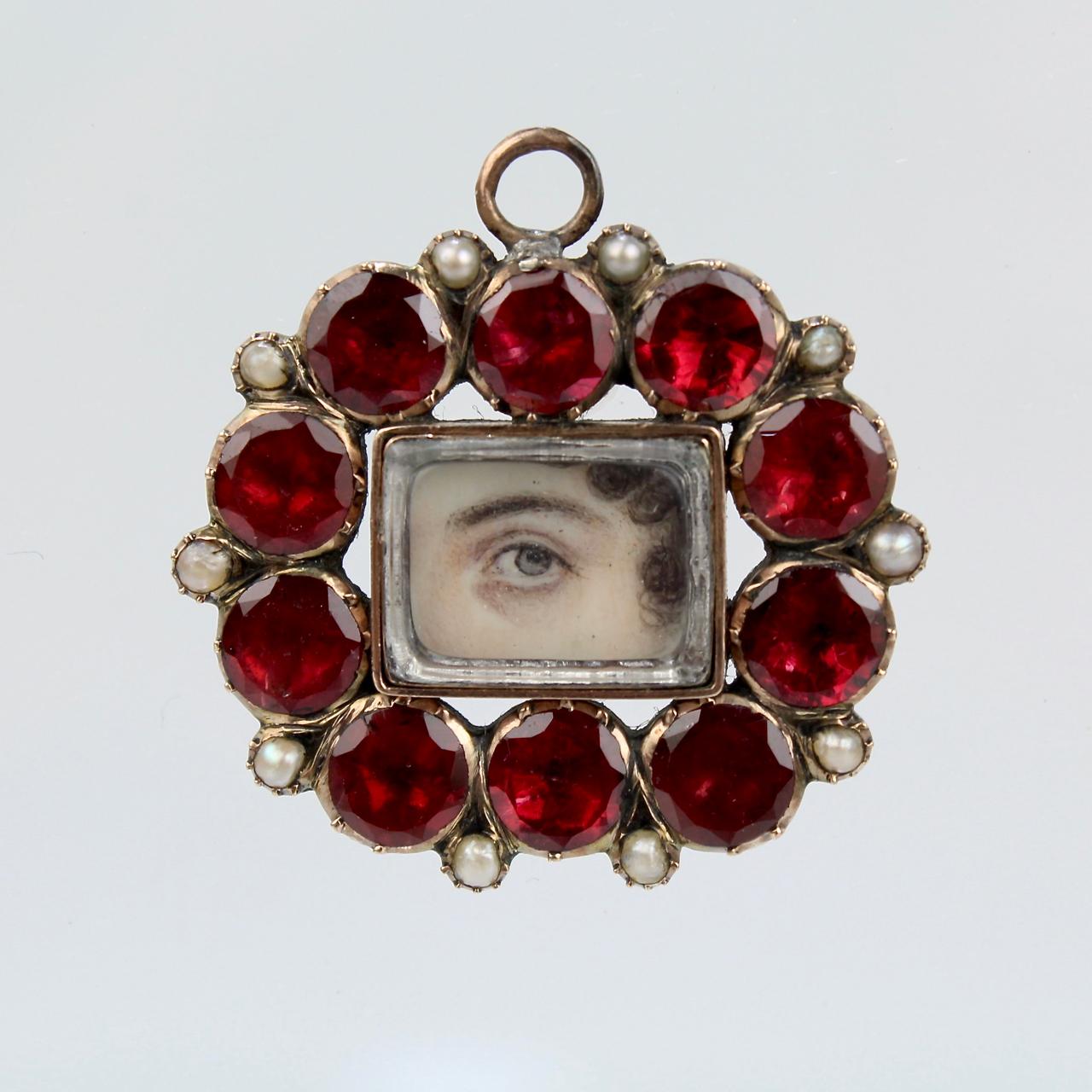 A very fine antique Georgian lover's eye pendant.

With a finely hand-painted lover's eye portrait surrounded by garnets and seed pearls in a low karat gold setting. The top is set with a loop for a jump ring to suspend it as a pendant.

In the