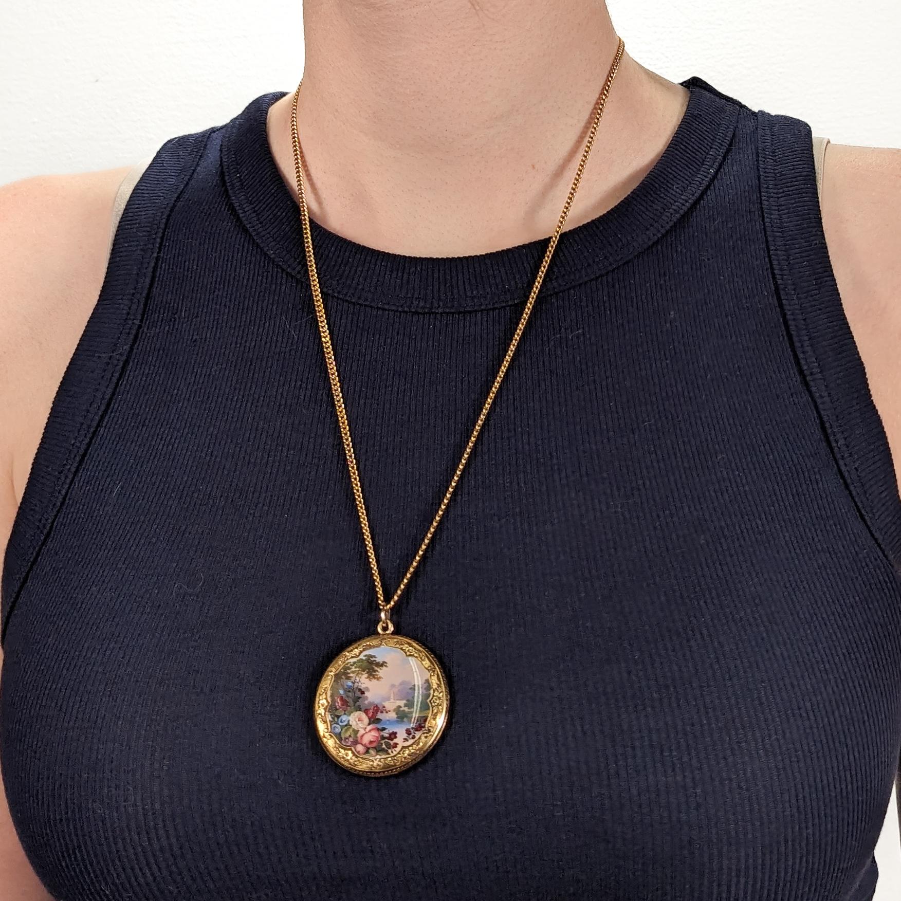 A fine antique compact shaped pendant for a necklace.

In 10k gold.

With a large central cartouche painted with a fine enamel landscape scene. The foreground having polychrome flowers and the background with a depiction of a river, a majestic
