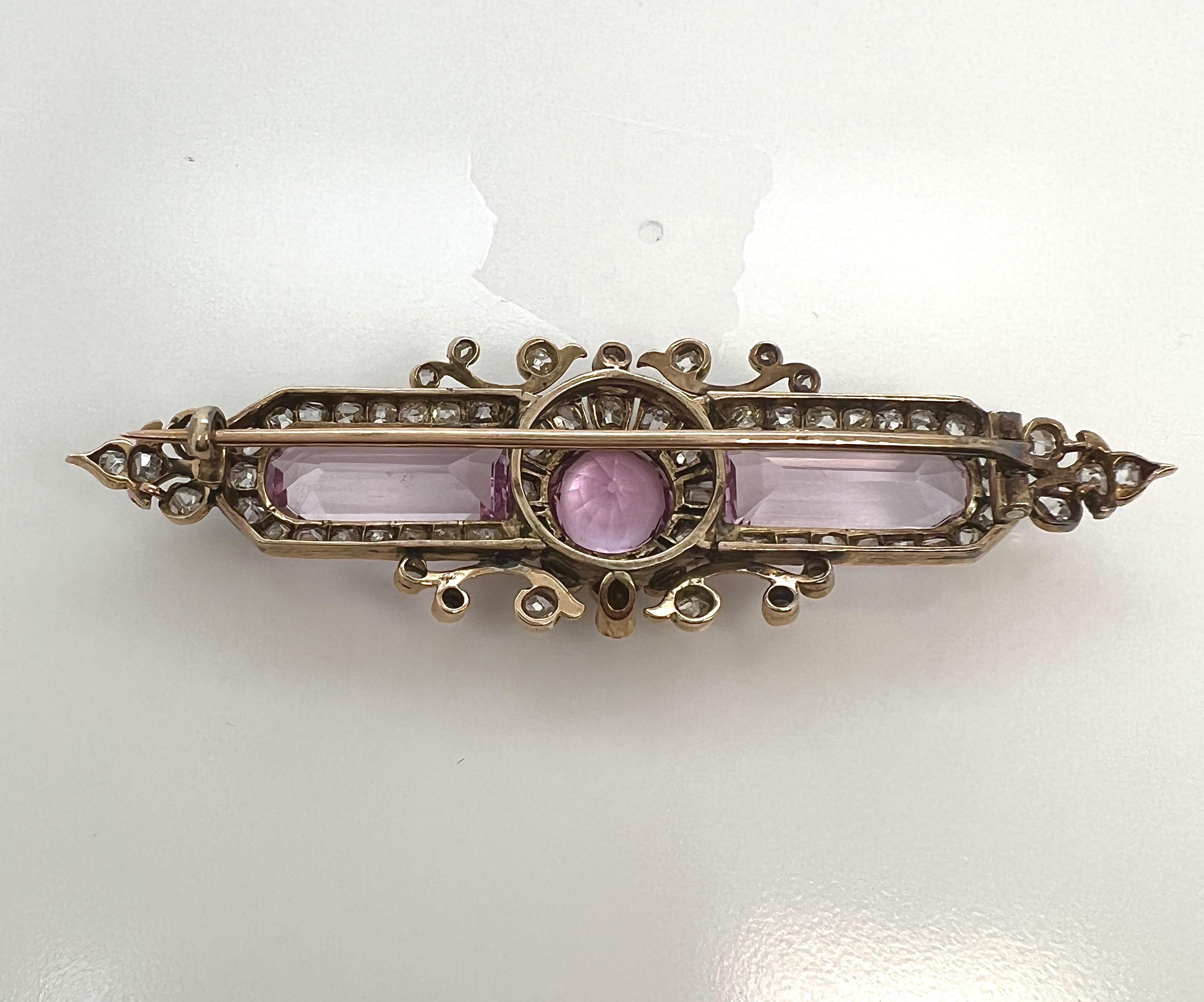 Antique Gold, Pink Topaz, and Diamond Brooch.

The bar brooch centering a round-cut pink topaz framed by old mine-cut diamonds and flanked by two rectangular-cut pink topaz further surrounded by old mine-cut diamonds; diamonds weighing approx. 2.30