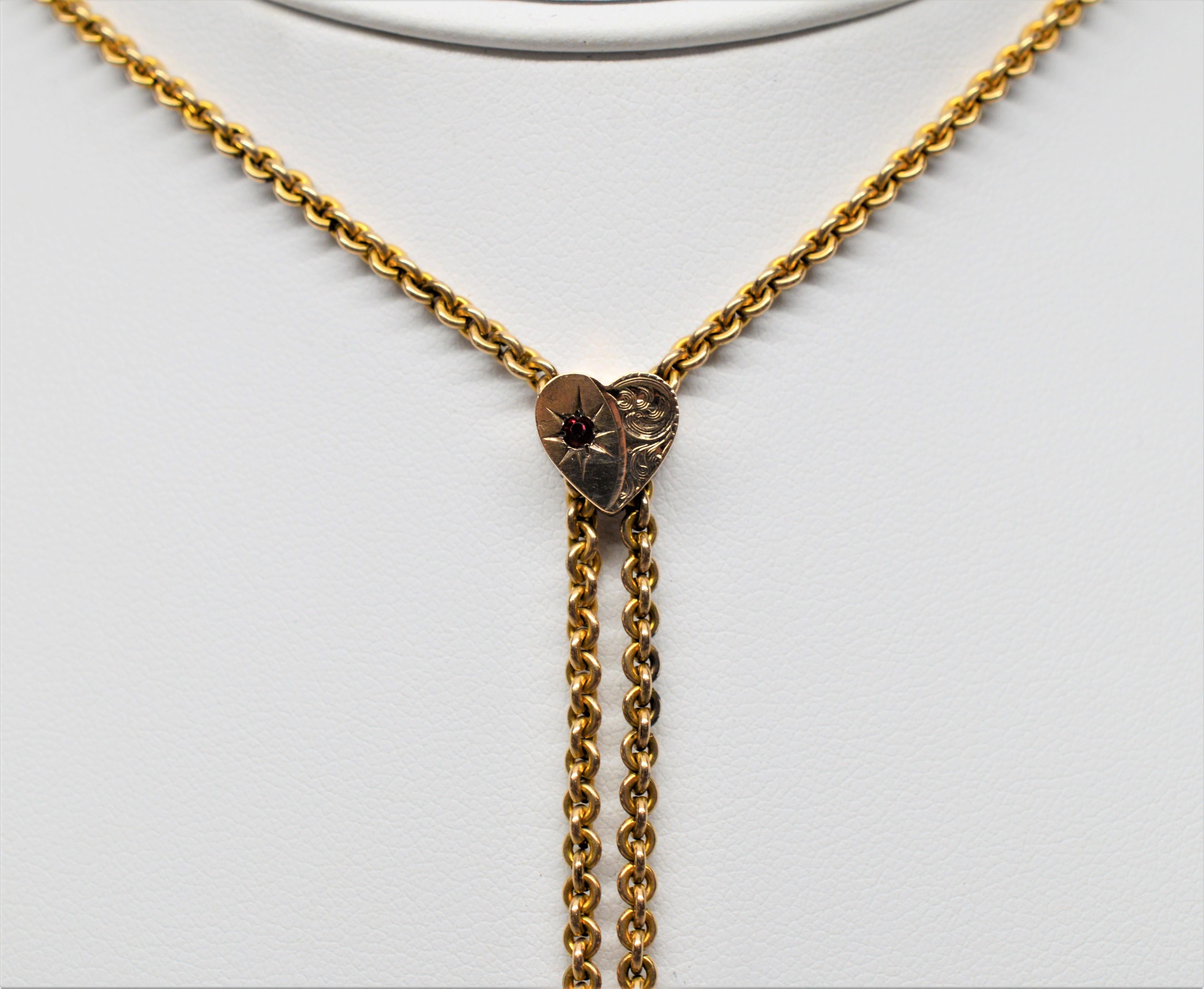 A lengthy fifty inches, this fourteen carat yellow gold plated ladies watch chain with fancy heart slide is a unique find and in unusually fine condition. Accented with a garnet gemstone the heart charm slides gracefully along the chain and adjusts