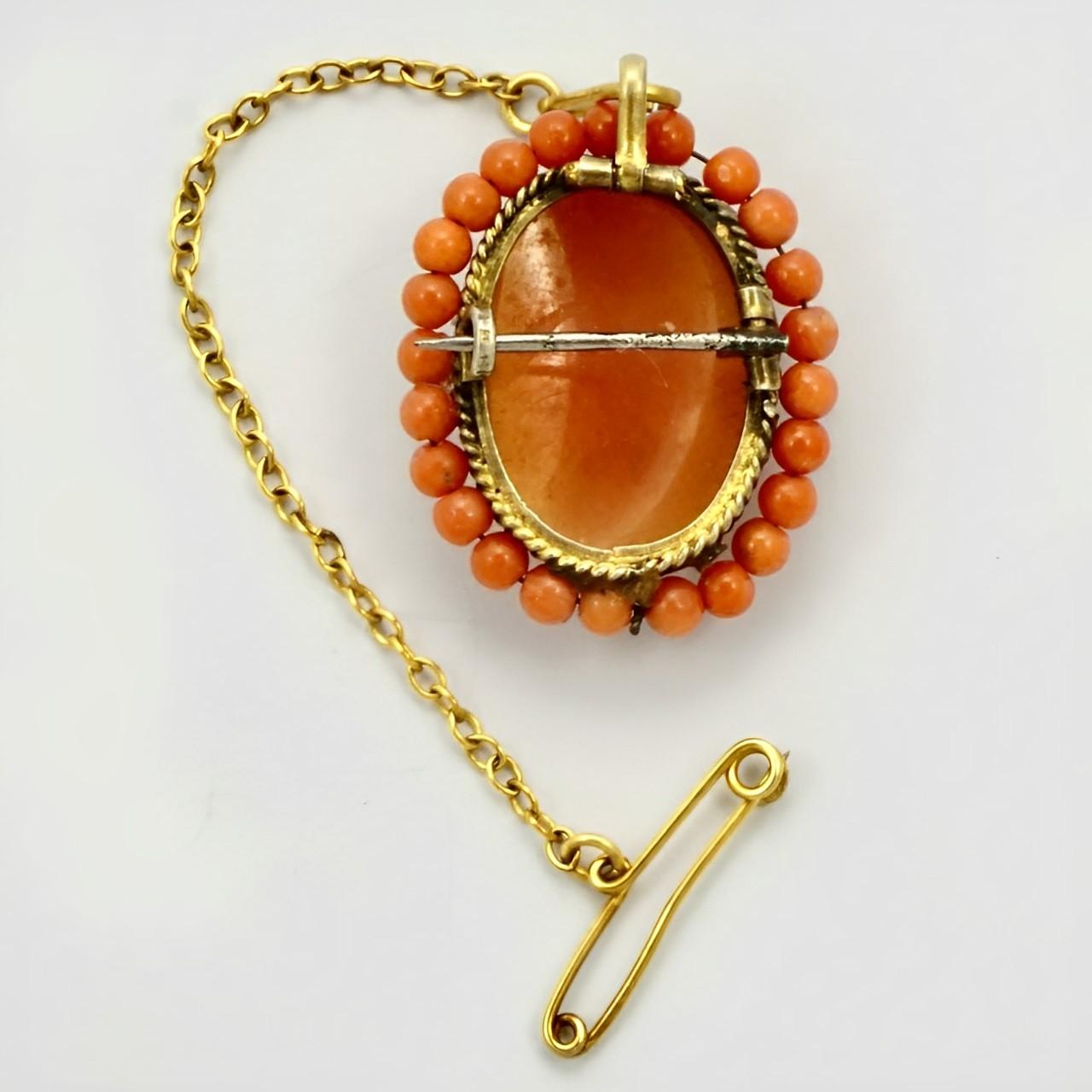 Beautiful gold plated shell cameo brooch, with rope twist detail and a coral bead surround. It has a safety chain. Measuring length 2.4 cm / .94 inch by width 2 cm / .78 inch. There is wear to the gold plating. The coral beads are on wire and