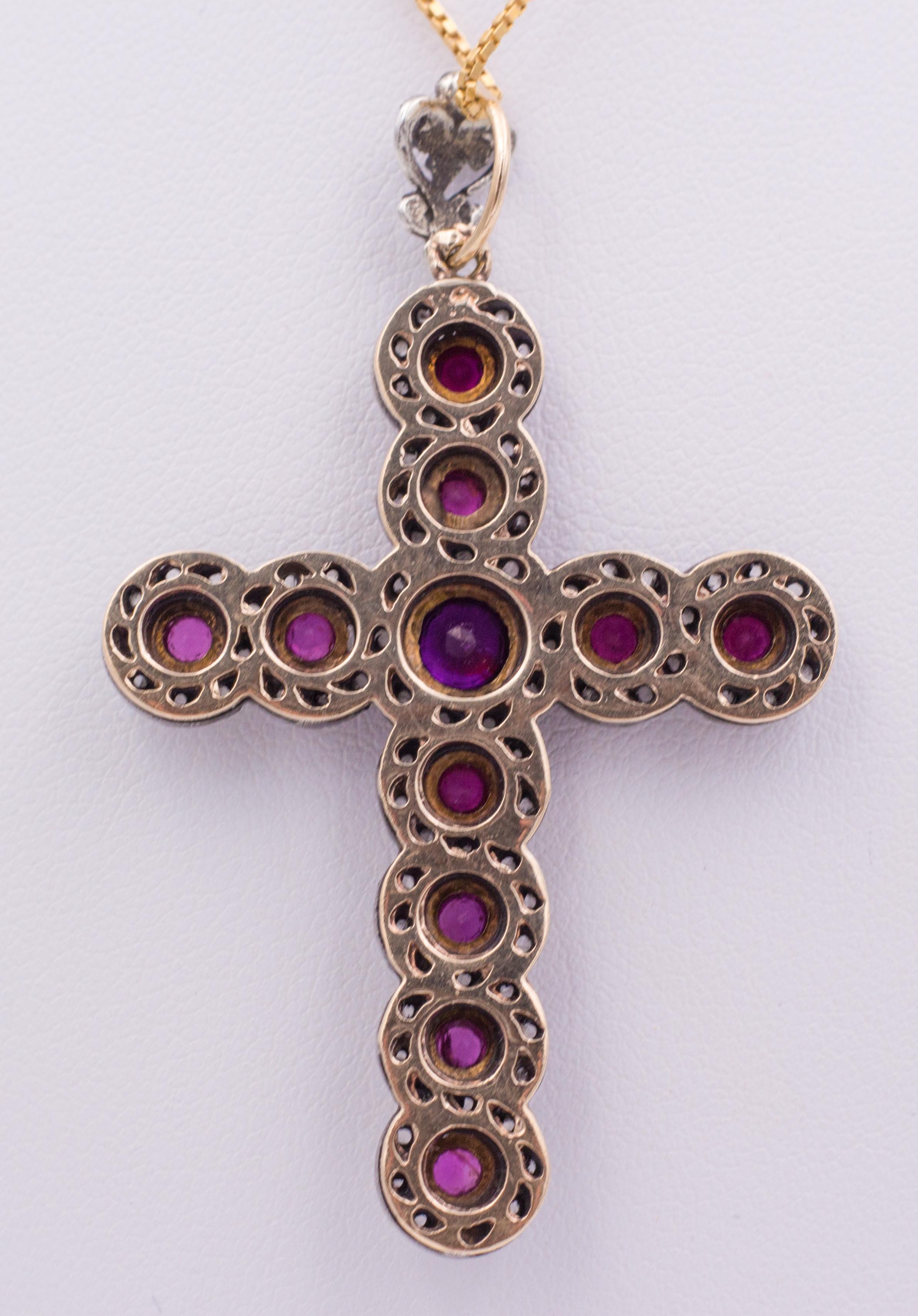 An antique gold crucifix pendant, dating from the early 20th Century: it has a very interesting undulating shape, and it is set with rubies and rose cut diamonds; the pendant is crafted in gold and silver throughout. 
The gold chain is not included