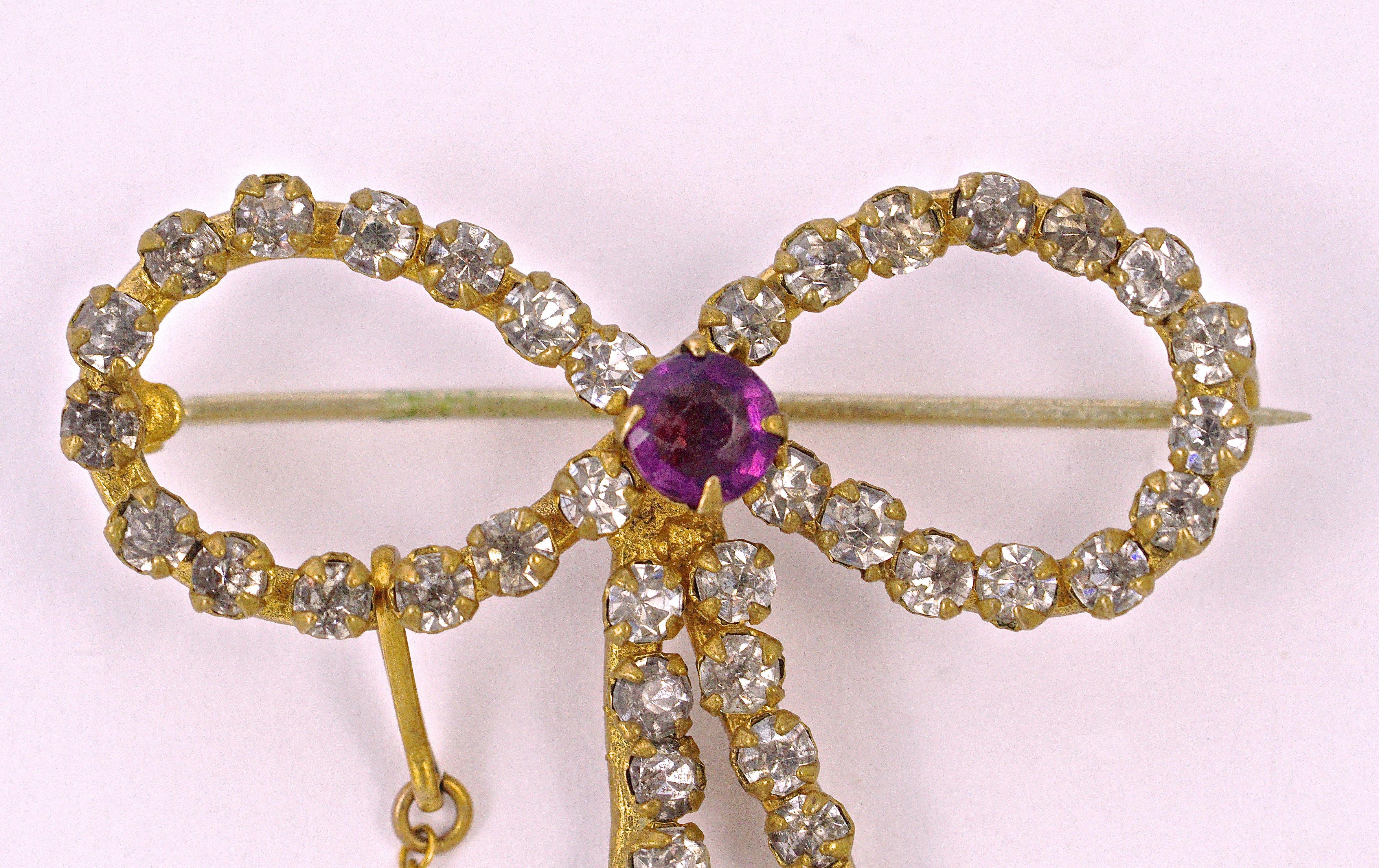 
Exquisite antique gold tone bow brooch set with clear sparkly paste stones, and a centre amethyst paste stone. Measuring length 3.4cm / 1.33 inches by width 2.2cm / .86 inches. The ends of the bow are rose gold tone and are hand engraved. The