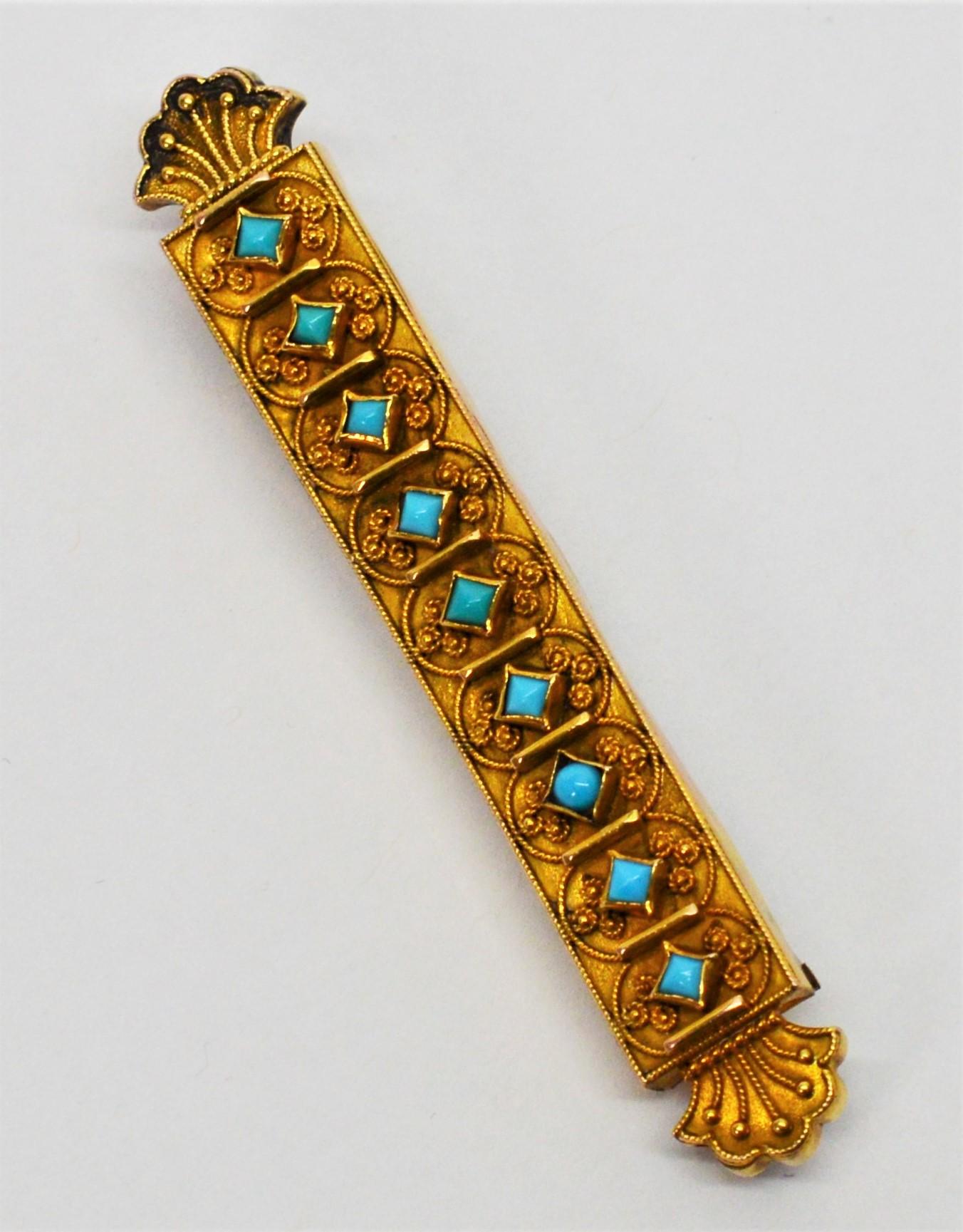Art Deco style, this ten carat antique yellow gold bar pin is accented with bezel set natural turquoise stones in patterned filigree. The 2-3/8 inch pin has decorative scroll ends and is secure with a rollover closure. The piece also is outfitted