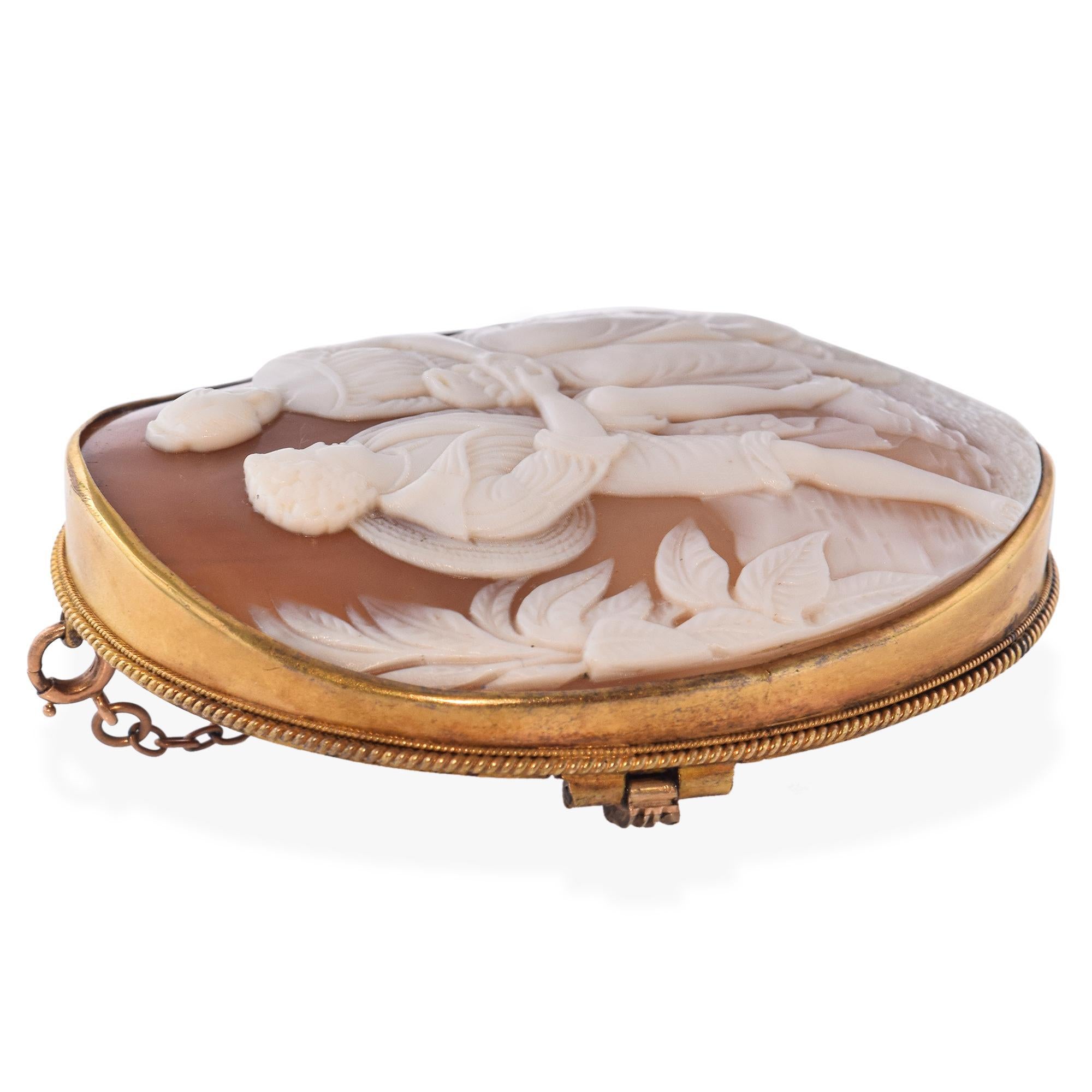 Este encantador broche camafeo antiguo de concha representa a una joven pareja provinciana en una tierna escena pastoril. Finamente tallada a mano y engastada en un cálido marco de oro vermeil, la pieza captura el romanticismo y la elegancia de la