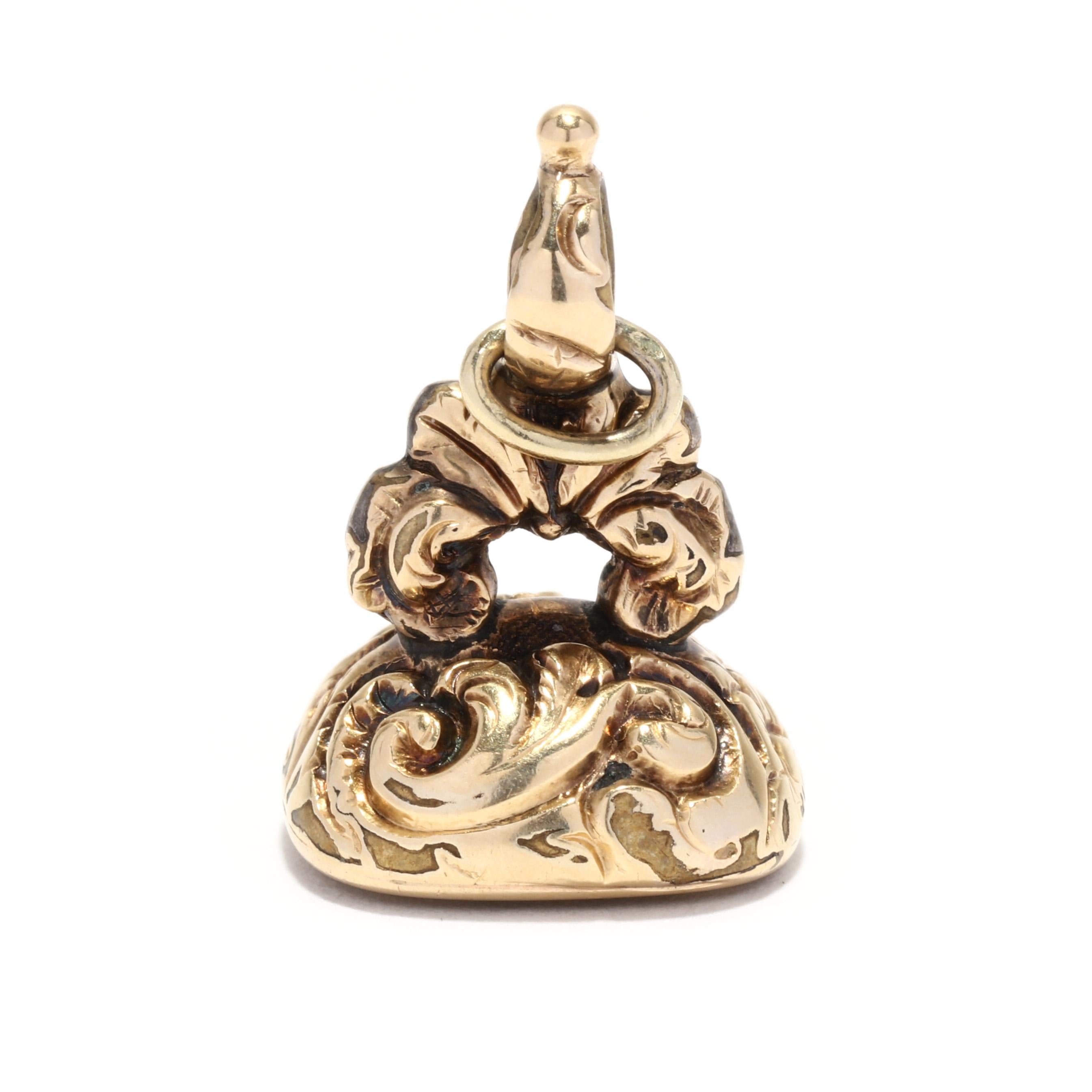 A Victorian 14 karat yellow gold engraved intaglio watch fob charm. This charm features a bezel set, cushion cut carved intaglio chalcedony depicting the profile of a man, set in an intricately engraved foliate and scroll motif watch fob.

Length: