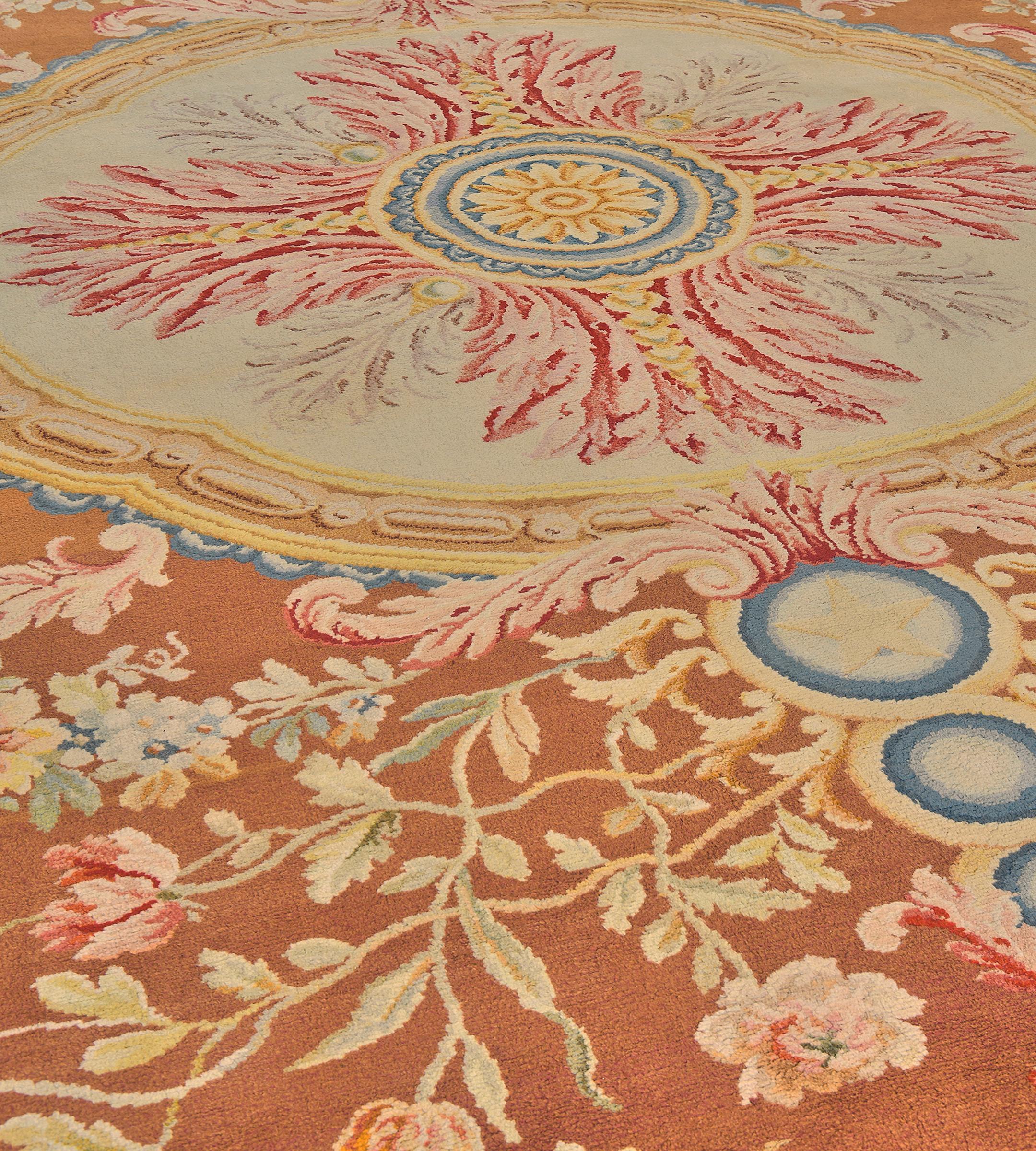 Cet ancien tapis de la Savonnerie française a un champ brun rougeâtre avec un grand rond central ivoire contenant une rosette centrale jaune d'or et ivoire entourée d'étroites bandes jaune d'or et bleu clair et émettant des gerbes de feuilles